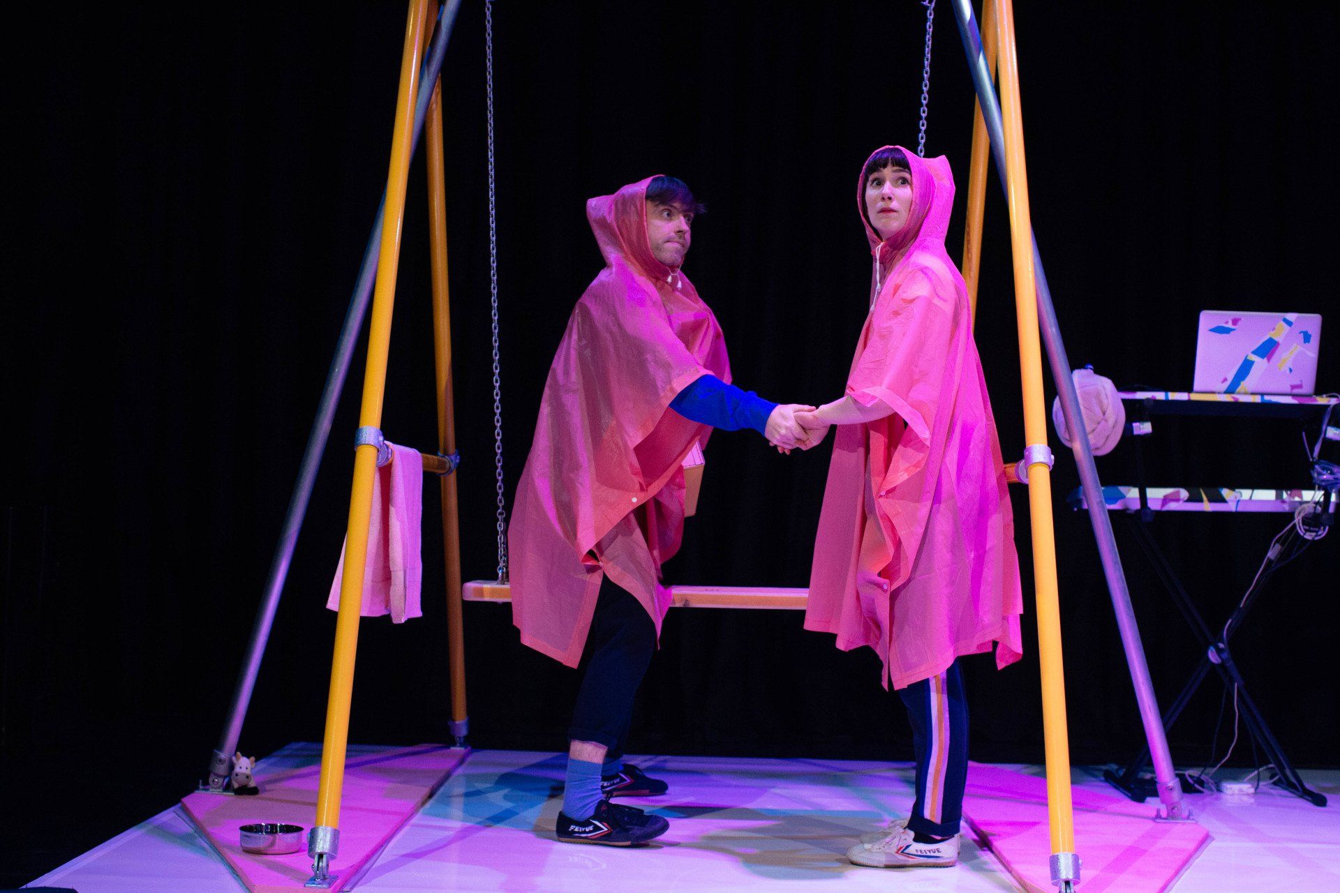 two people in pink ponchos are shaking hands on a swing .