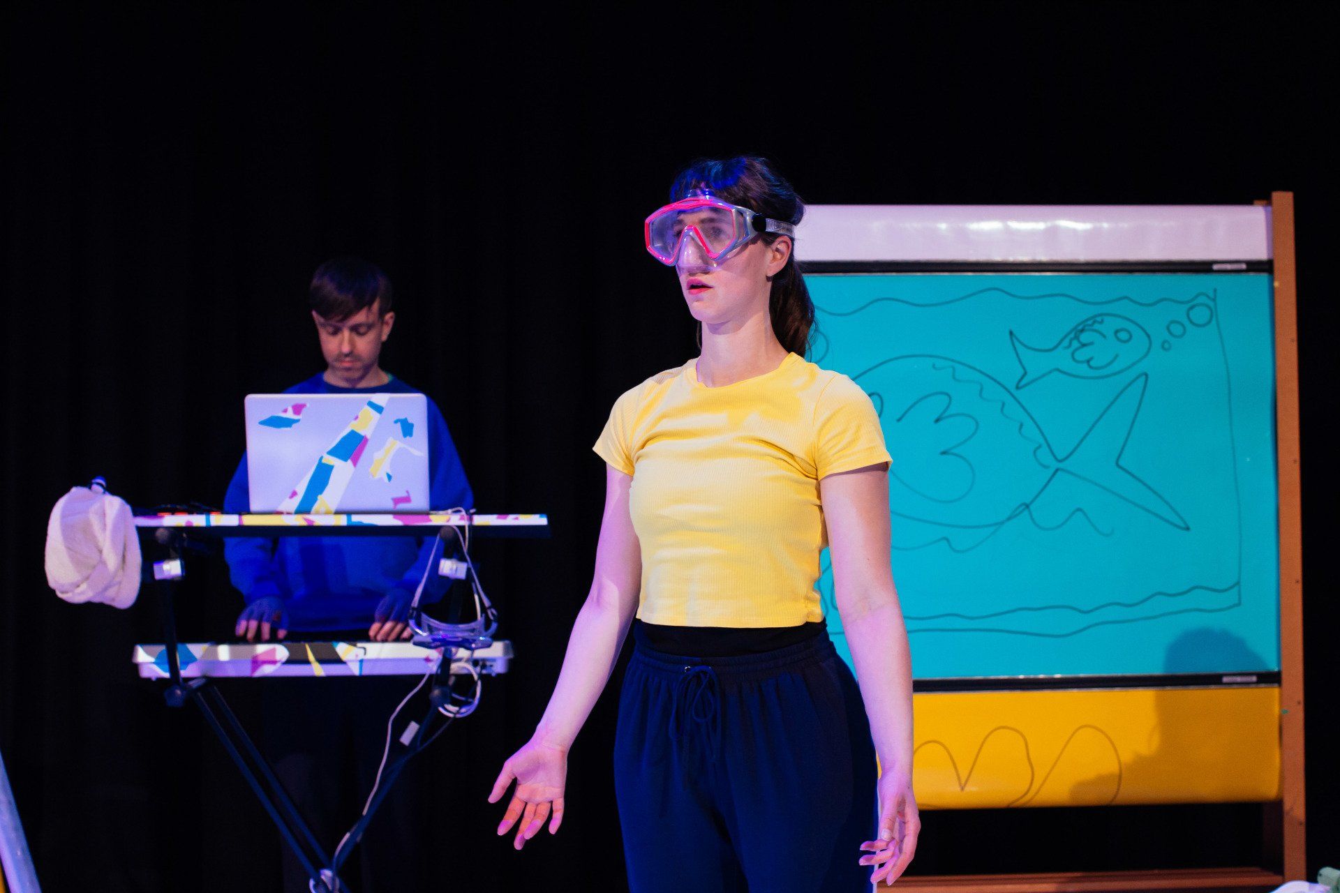 a woman wearing goggles is standing on a stage in front of a man playing a keyboard .