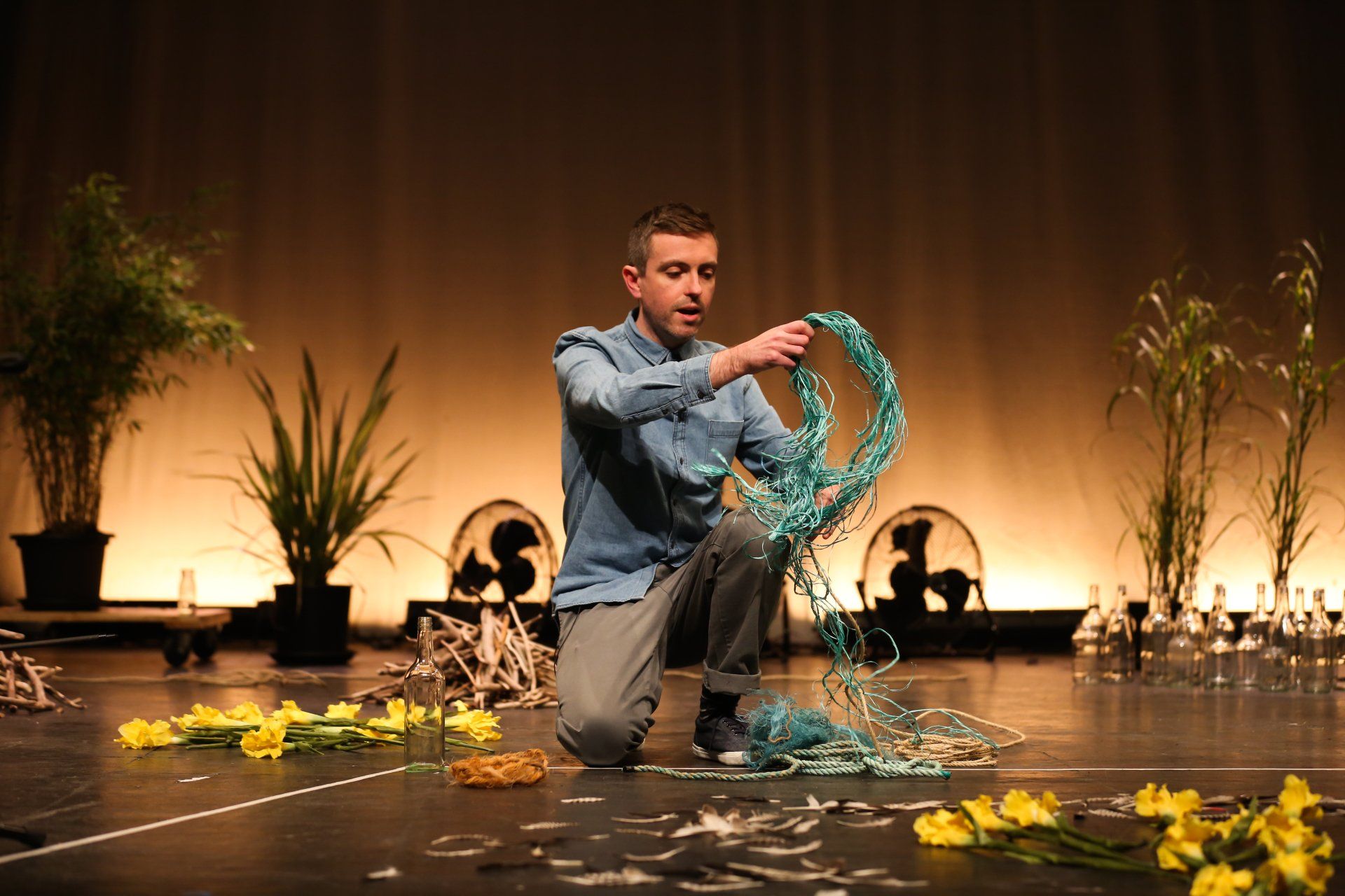 A man is kneeling on the floor on a stage holding a rope.