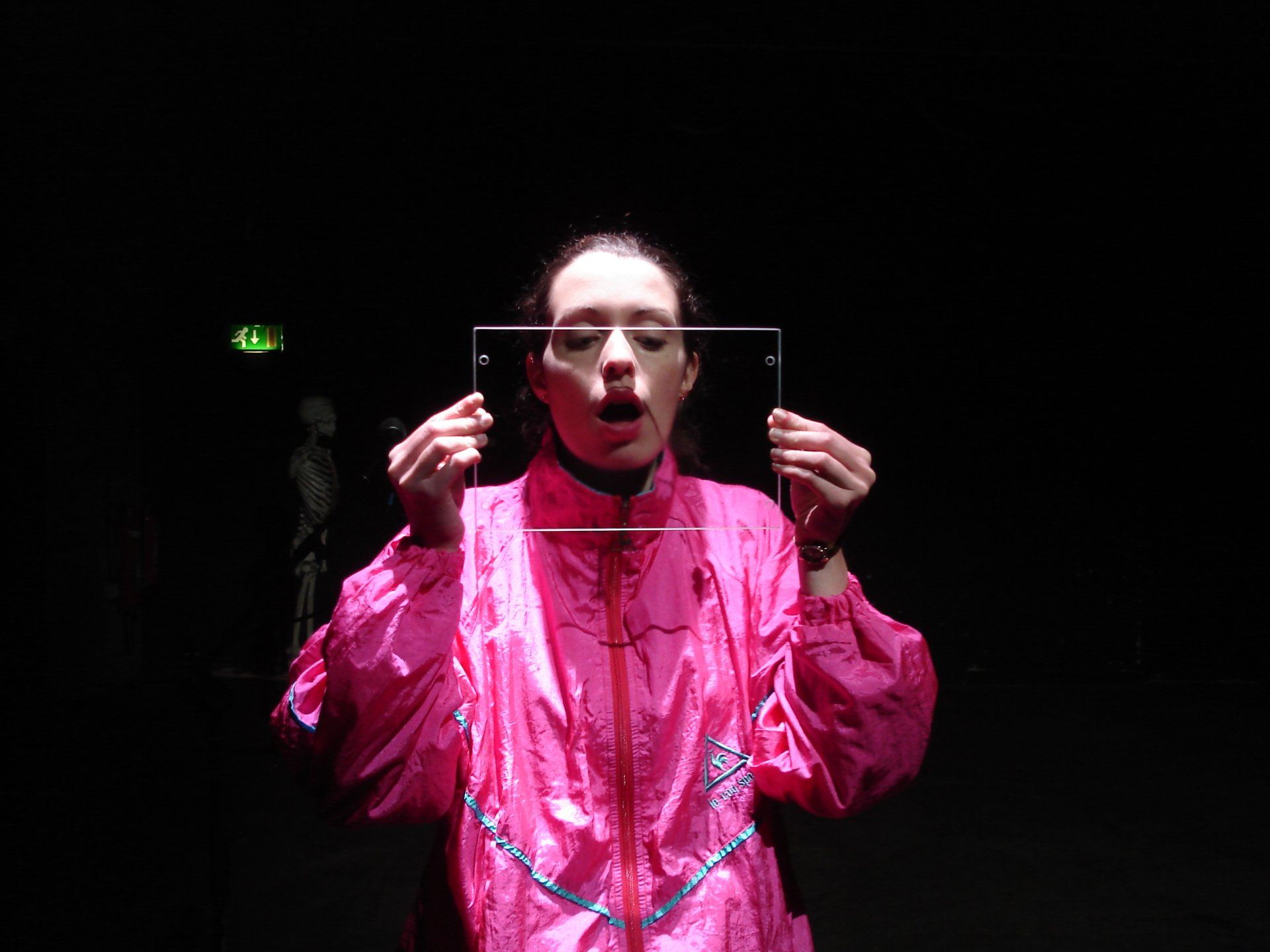 a woman in a pink jacket is holding a piece of glass in front of her face .