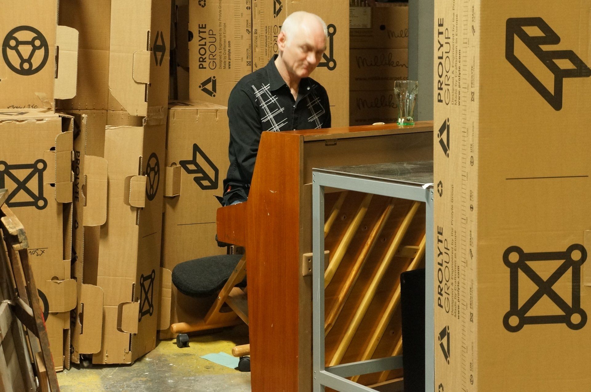 a man is playing a piano in a room filled with cardboard boxes