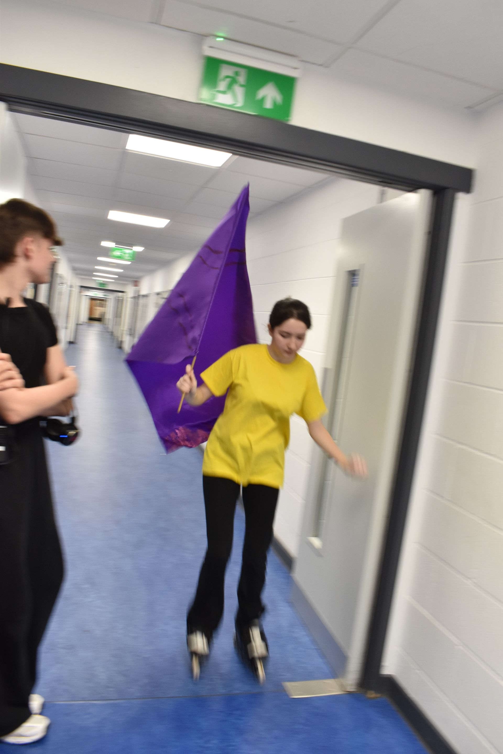A girl in a yellow shirt is holding a purple flag in a hallway