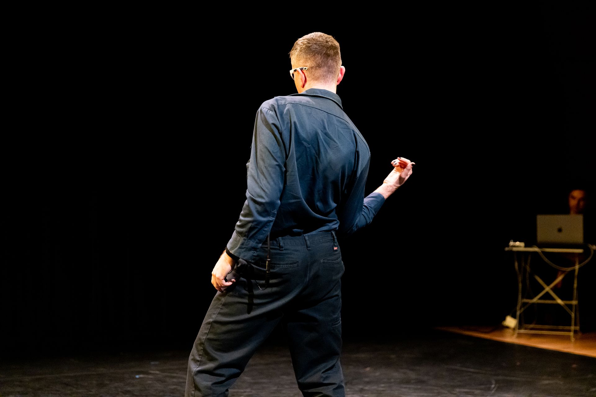 A man in a blue shirt and blue trousers is standing on a stage.