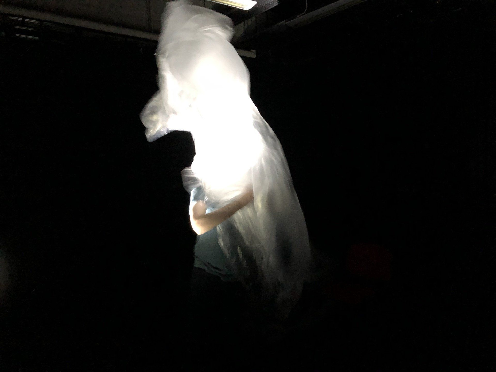 a person is standing in the dark with a white cloth hanging from the ceiling .
