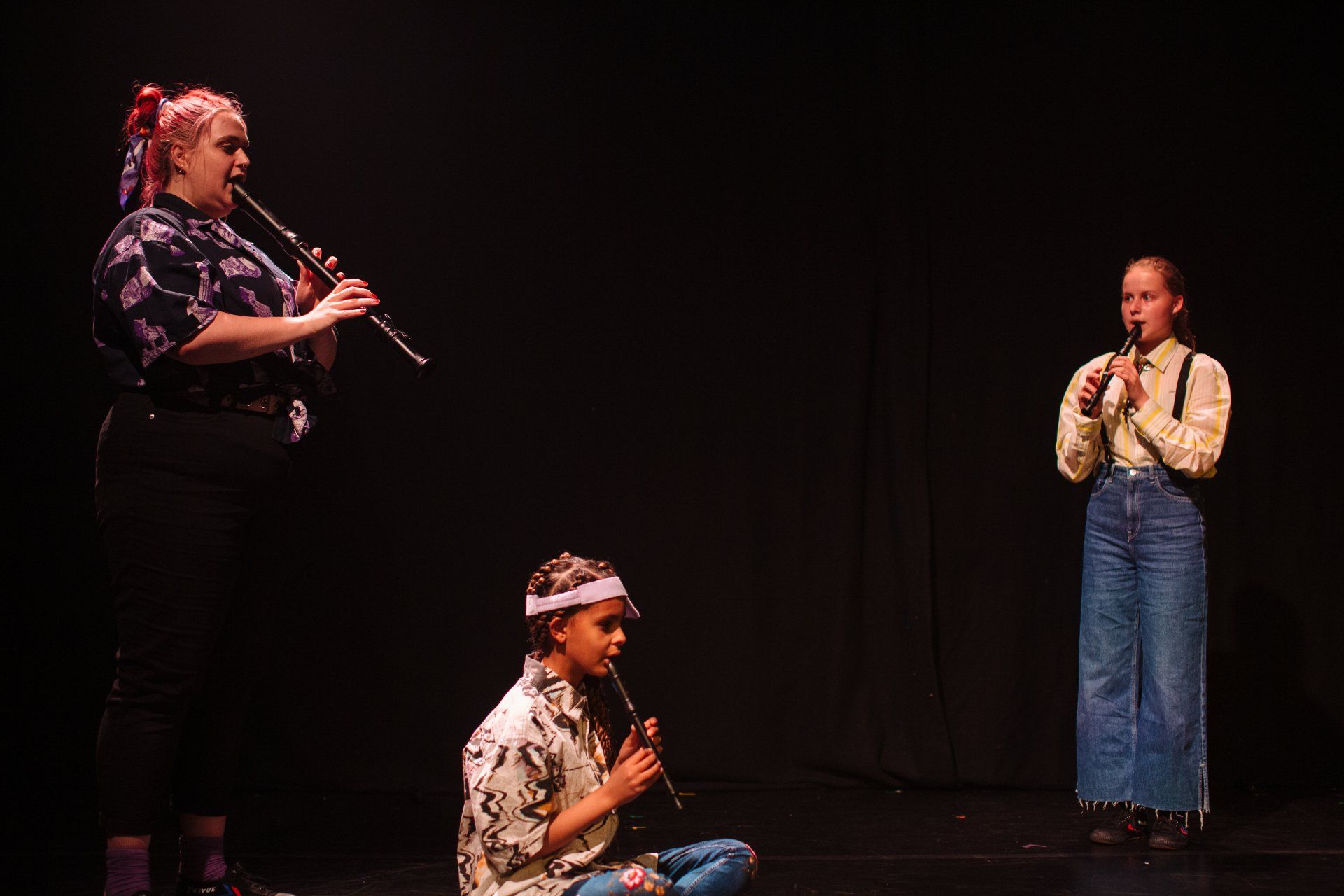 a woman is playing a recorder and two girls are singing on a stage .