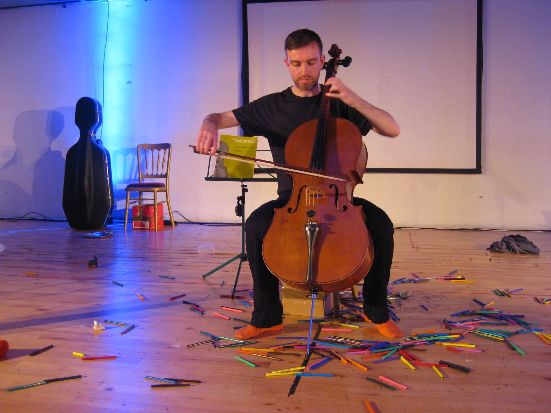 a man playing a cello on a stage surrounded by pencils