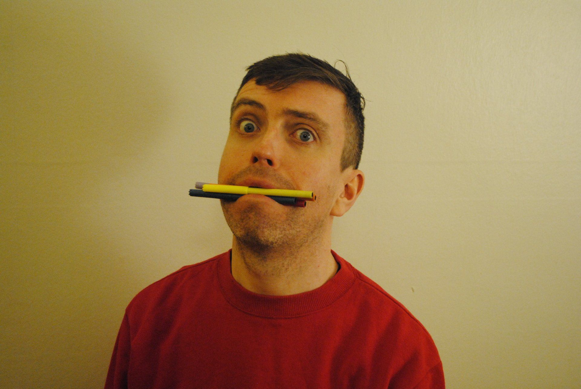 a man in a red sweater is holding a pen in his mouth .