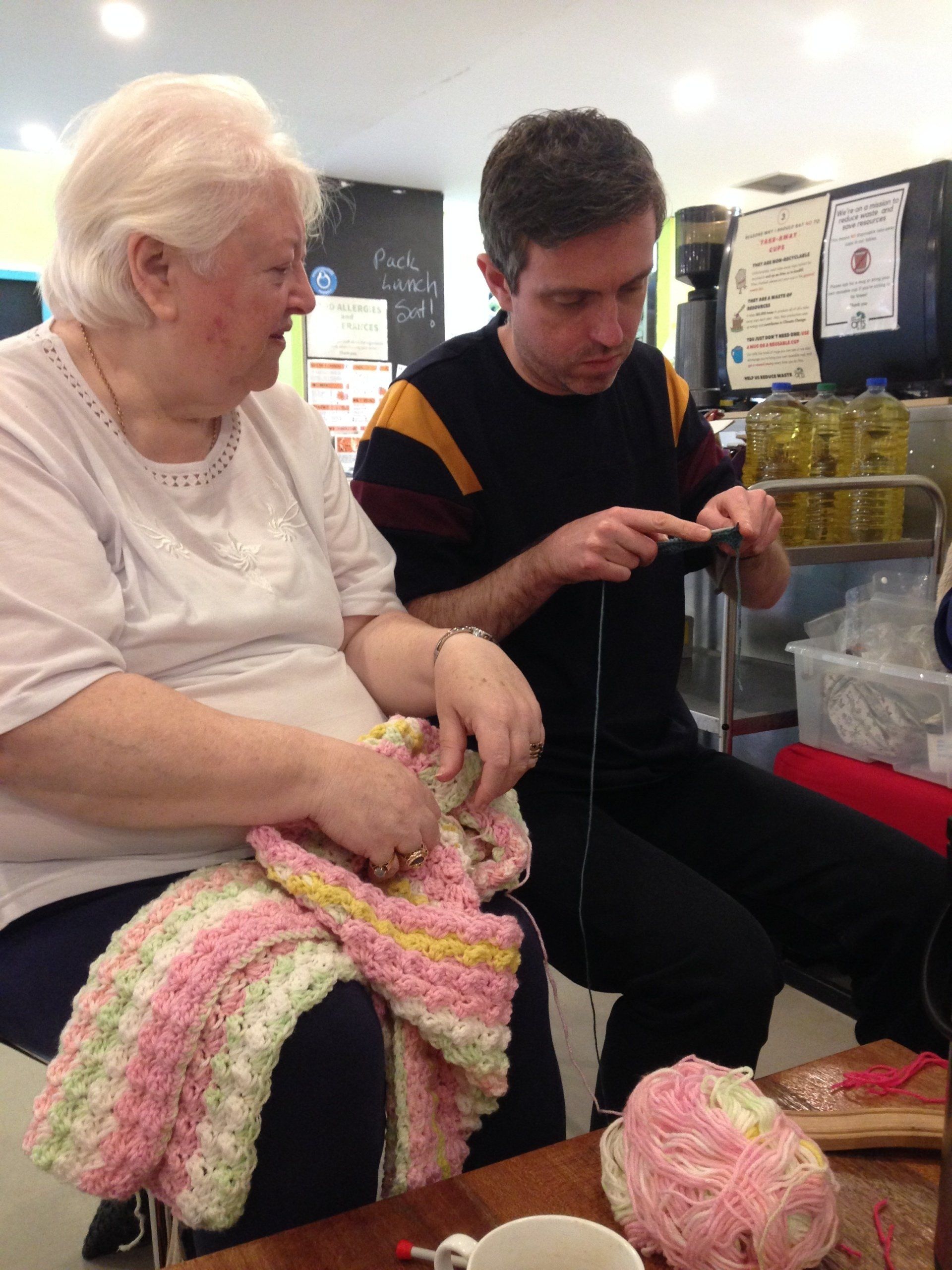 A man and a woman are knitting together at a table.