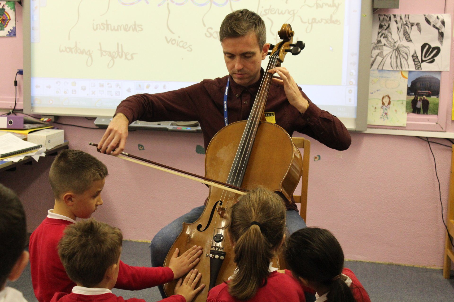 a man is playing a cello in front of a group of children in a classroom .