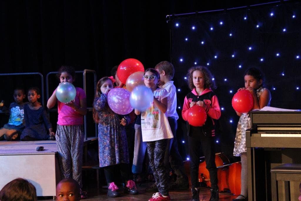 A group of children are blowing up balloons on a stage.