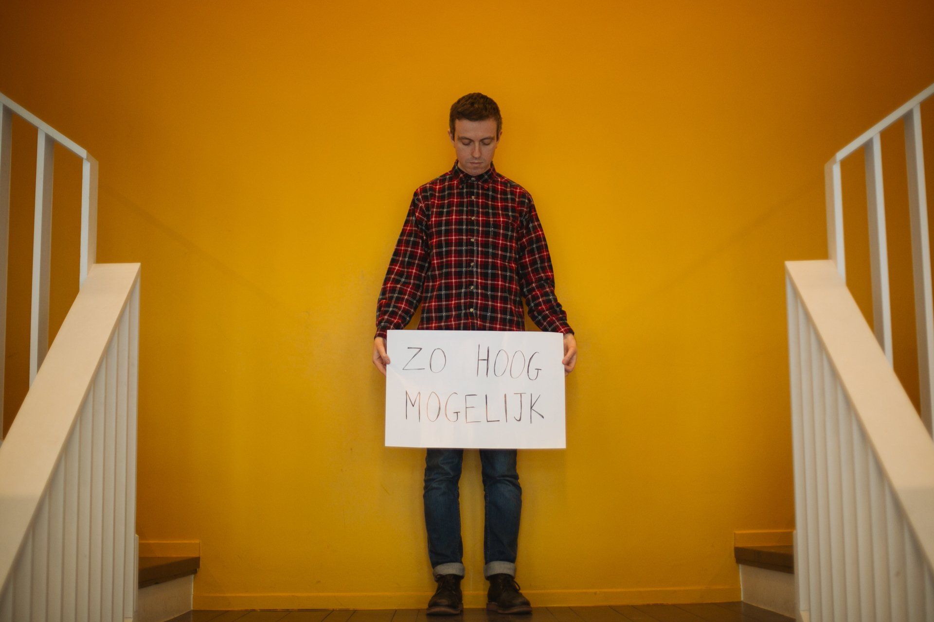 a man in a plaid shirt is holding a sign in front of a yellow wall .