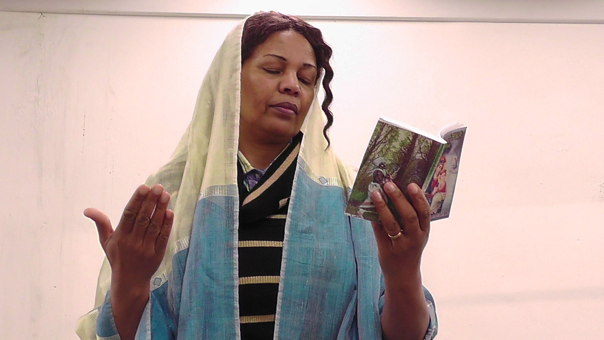 a woman wearing a head scarf is holding a book in her hands .