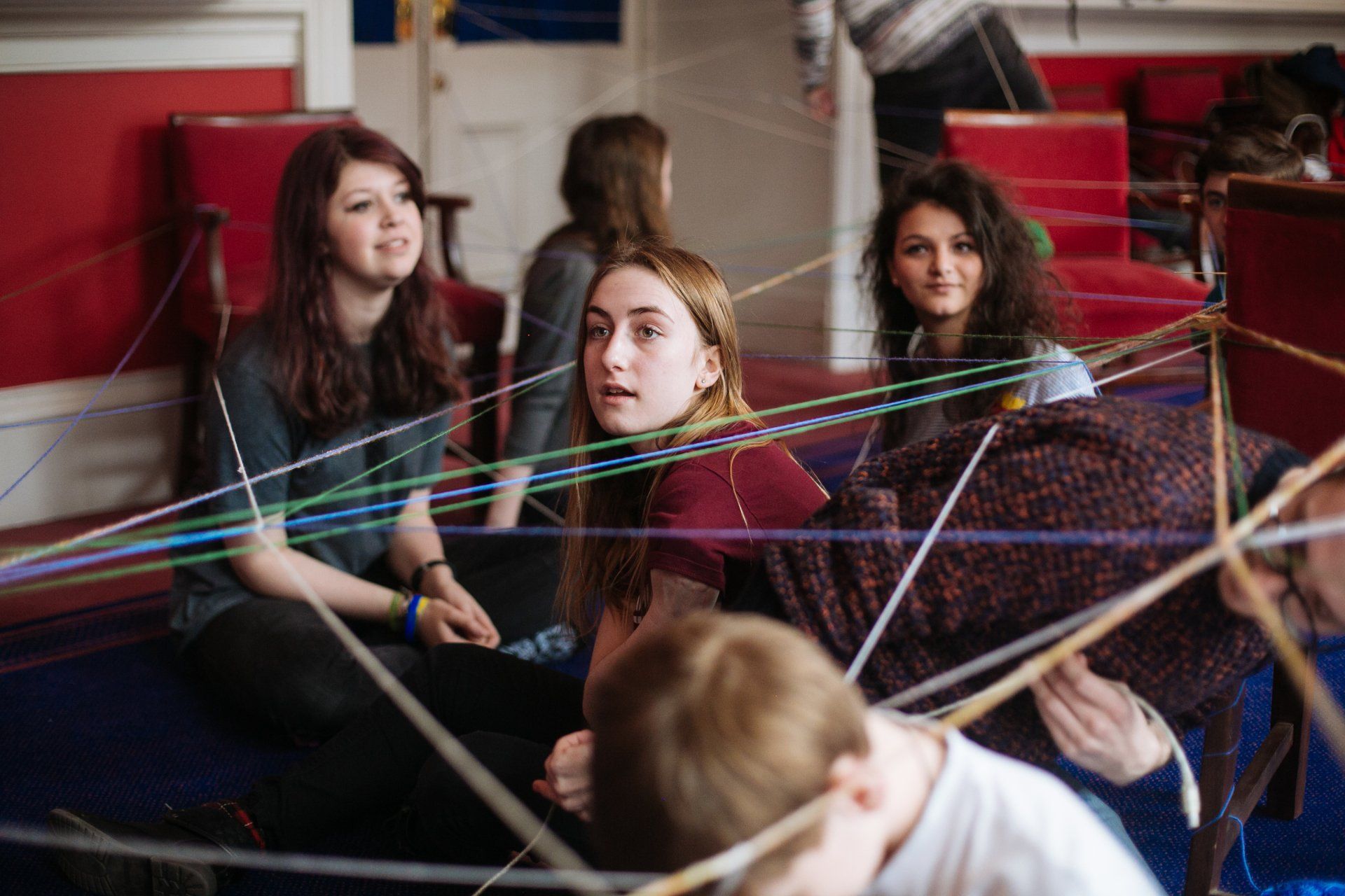 a group of people are sitting on the floor playing with yarn .