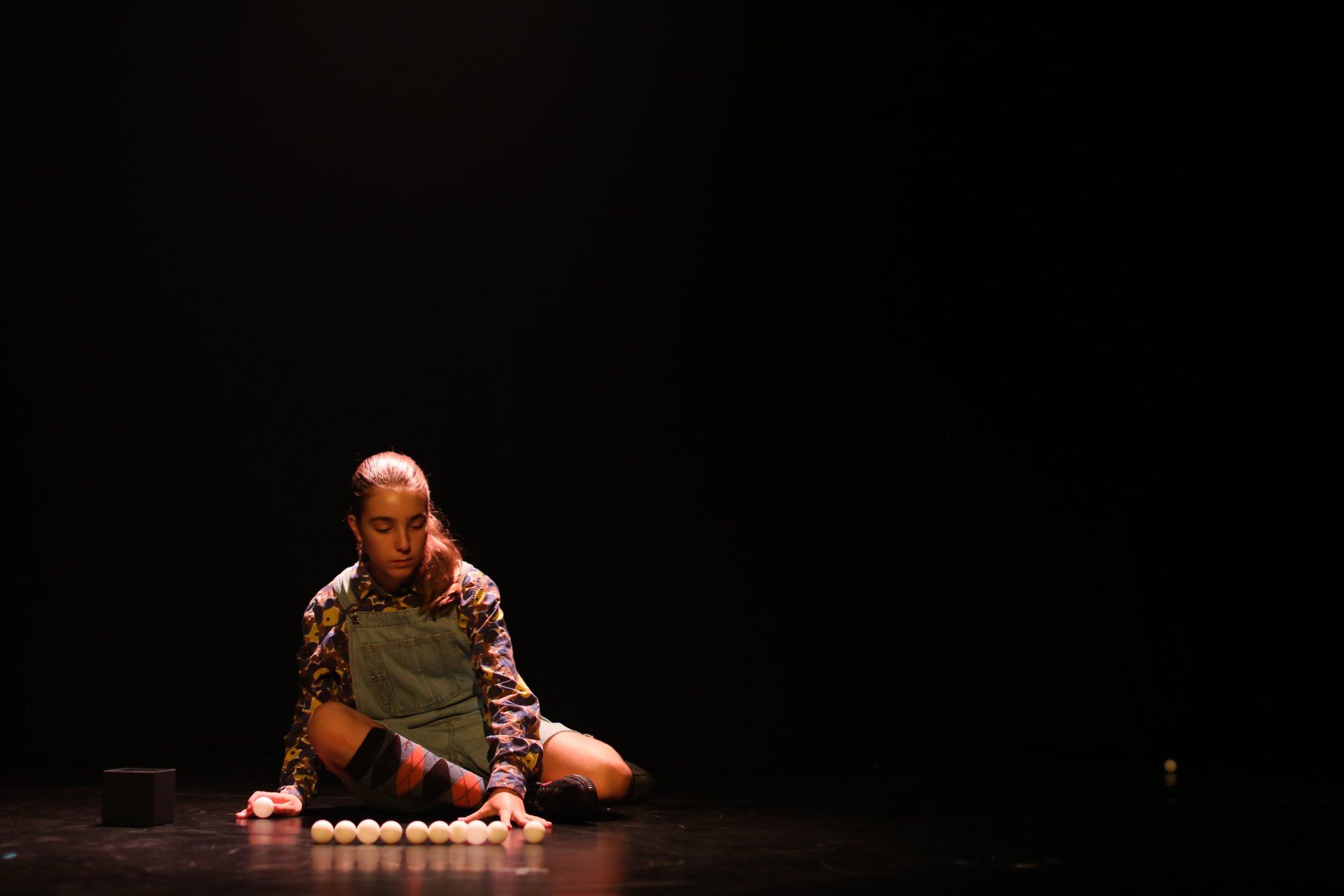 a girl is sitting on the floor on a stage holding a bunch of ping pong balls .