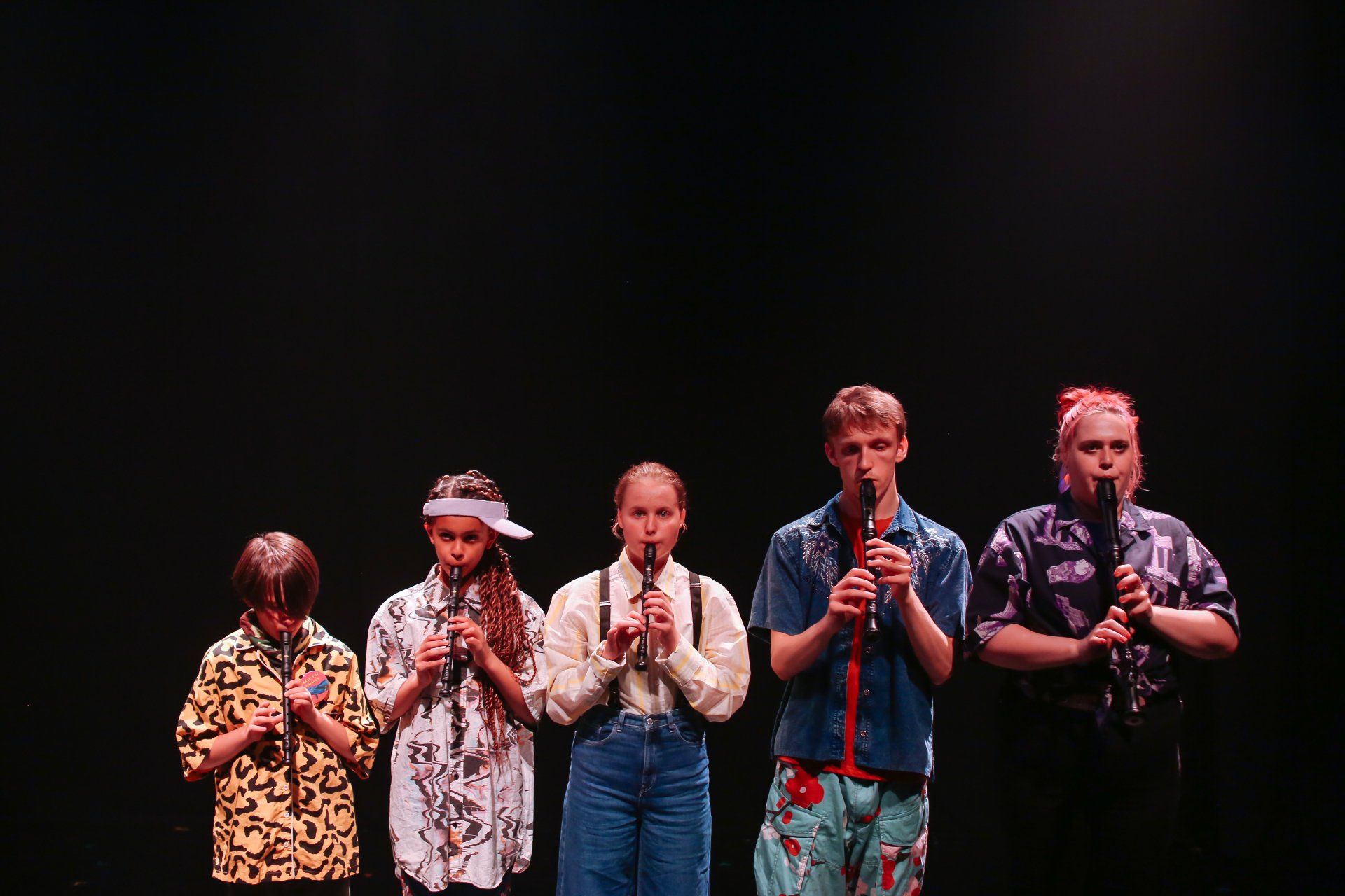 a group of young people are standing next to each other on a stage playing recorders .