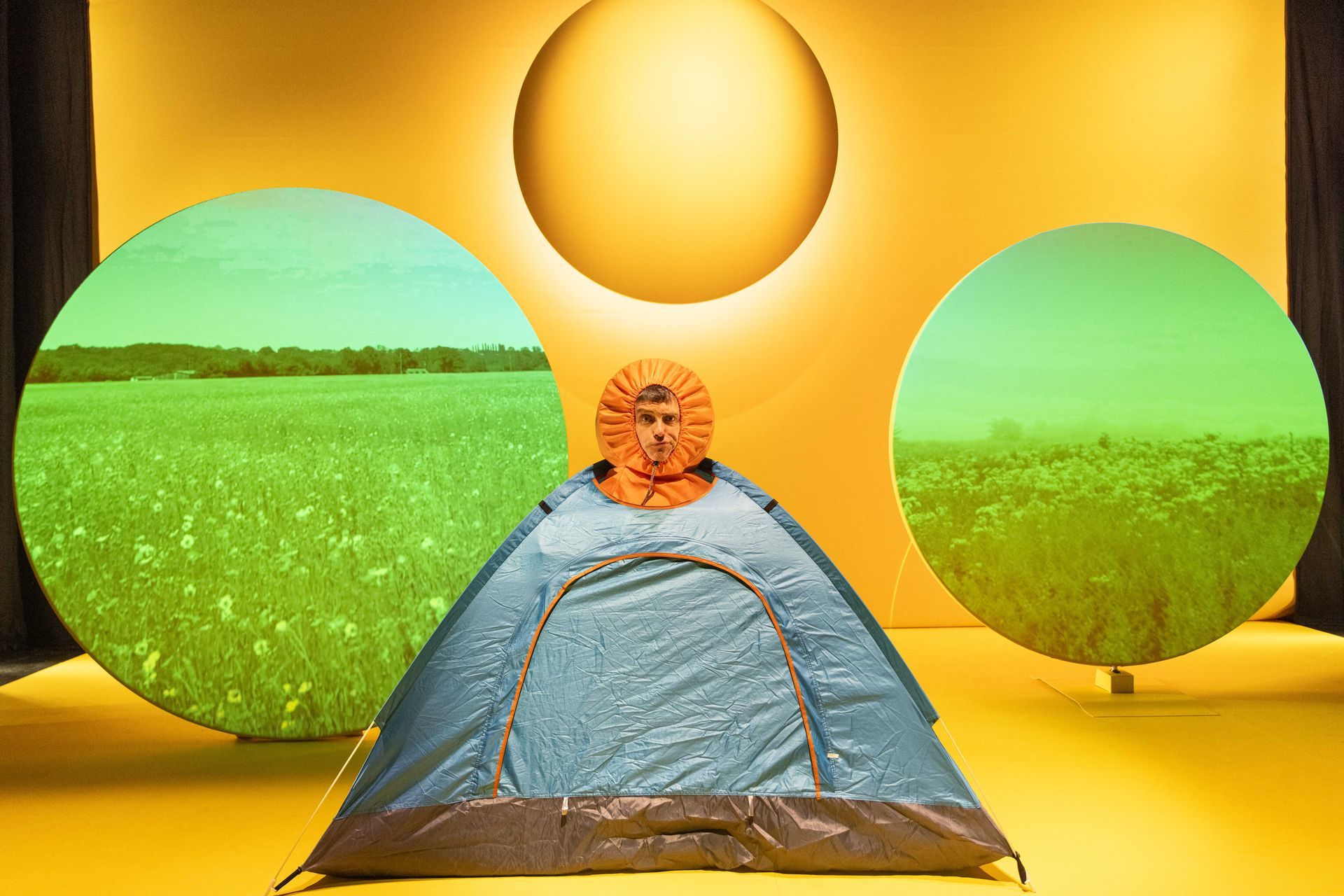 A person wearing an orange headdress has his head poking out of a tent.