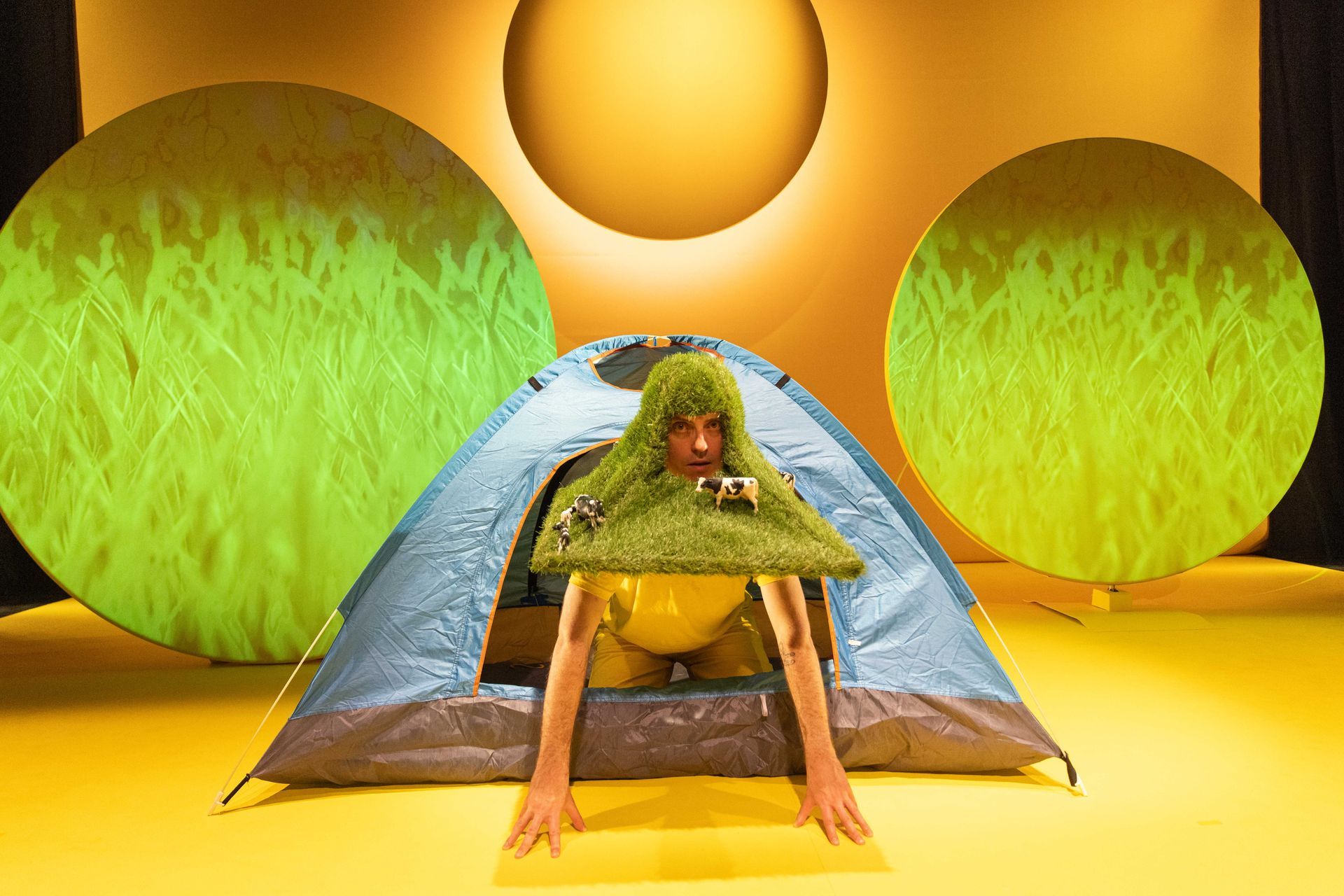 A person is emerging from a tent with a strange grassy headdress on their head.