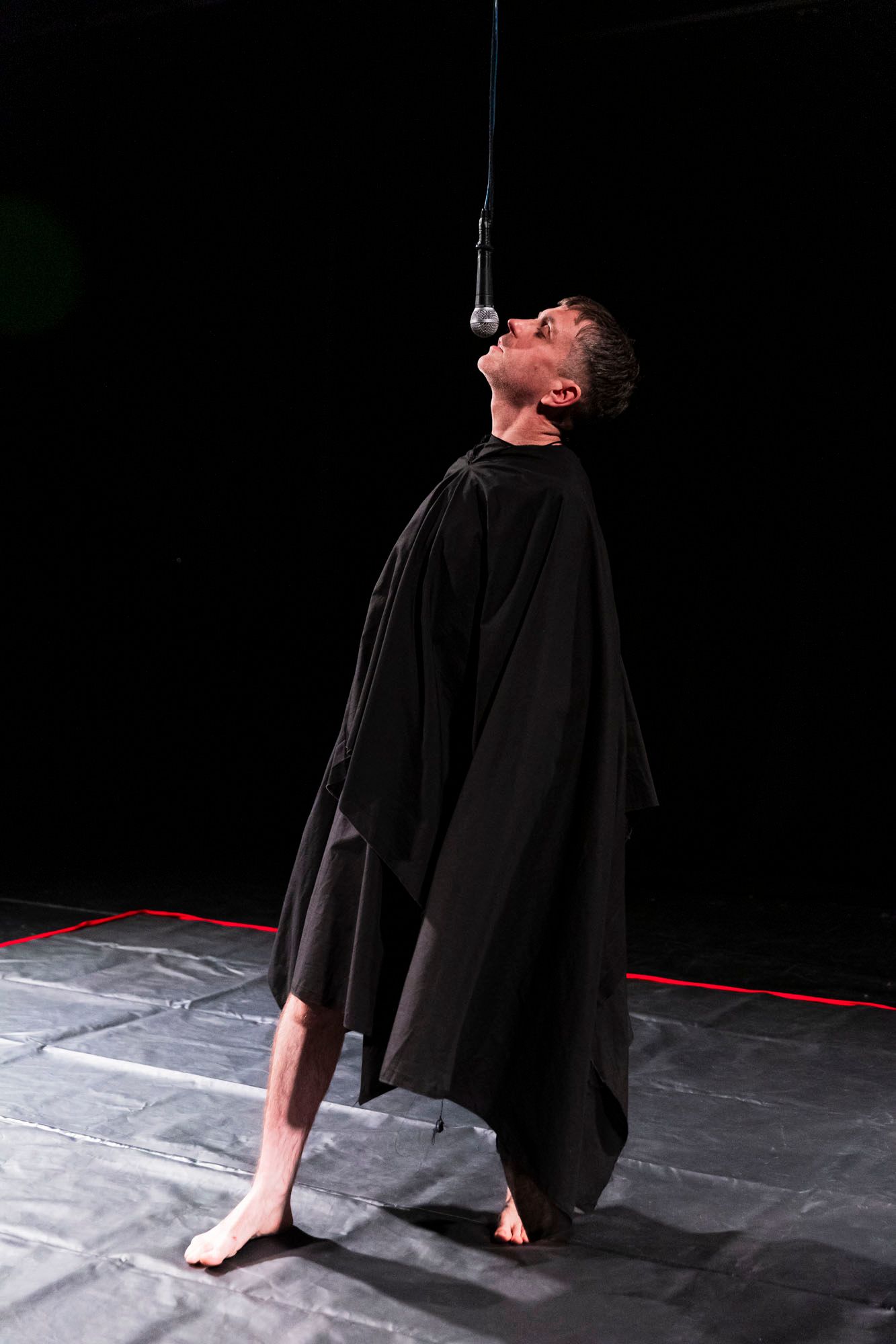 A man in a black cape is speaking into a suspended microphone.