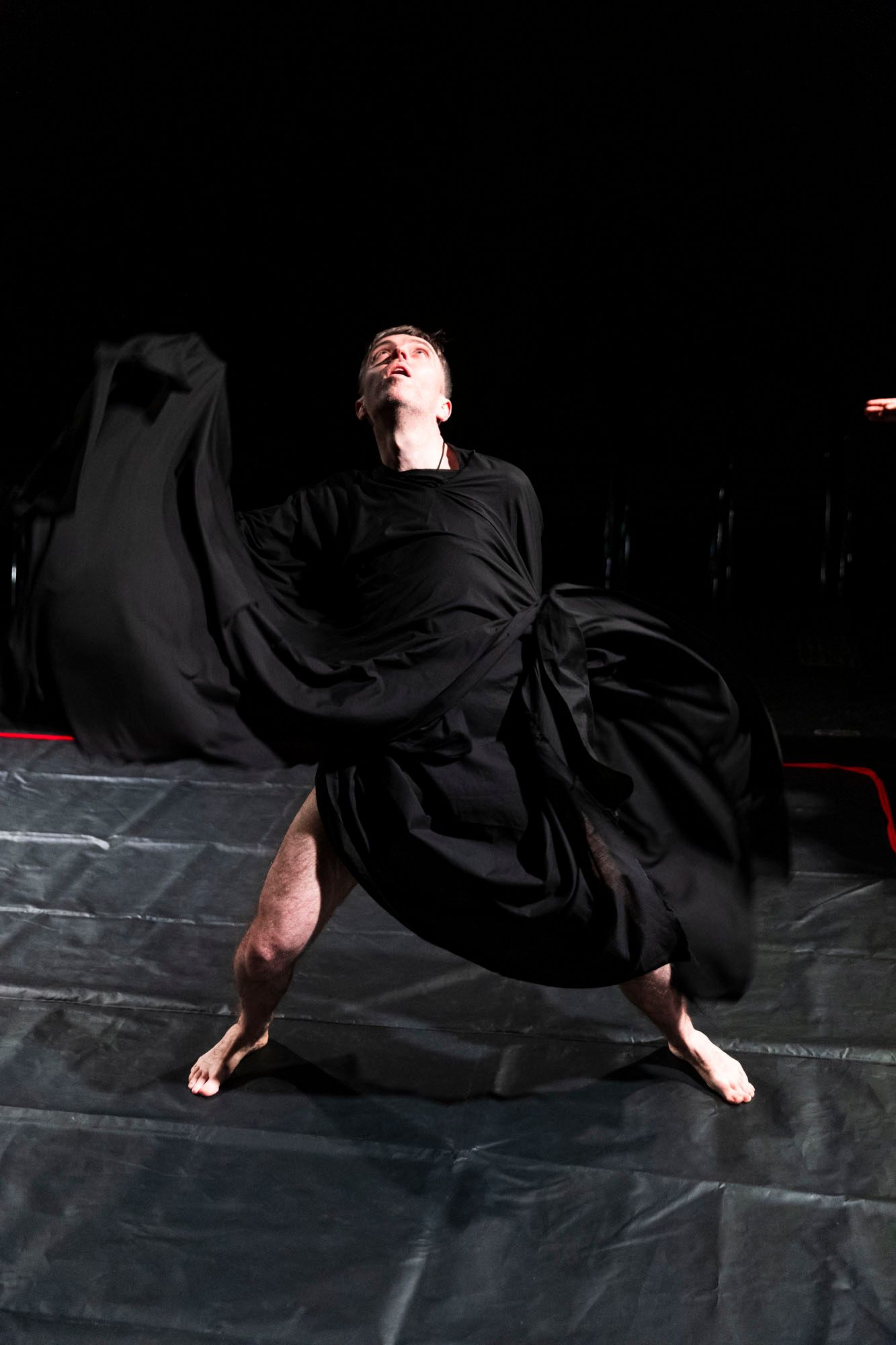 A man in a black dress is dancing on a stage.