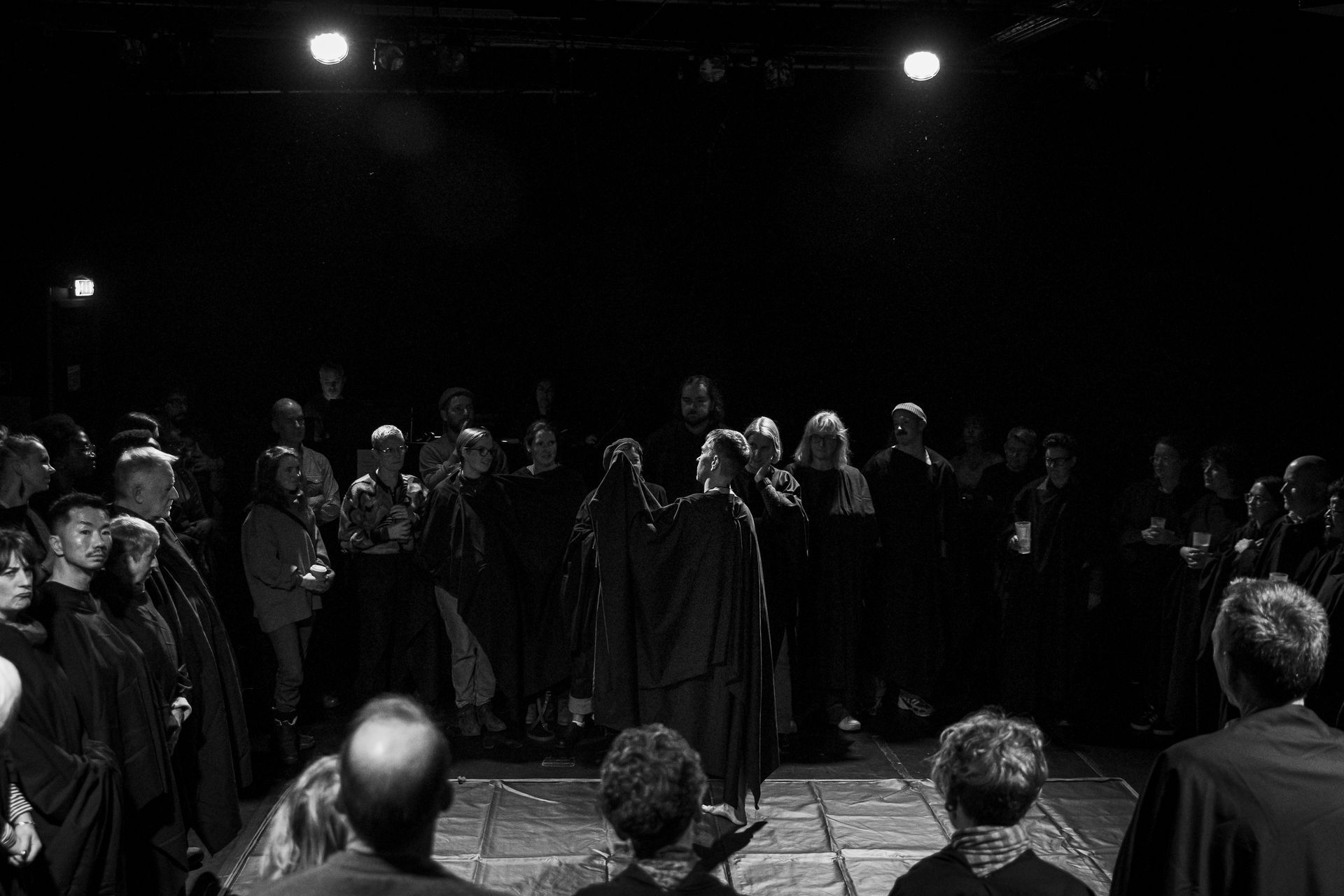 A group of people are standing in a circle on a stage in a dark room.