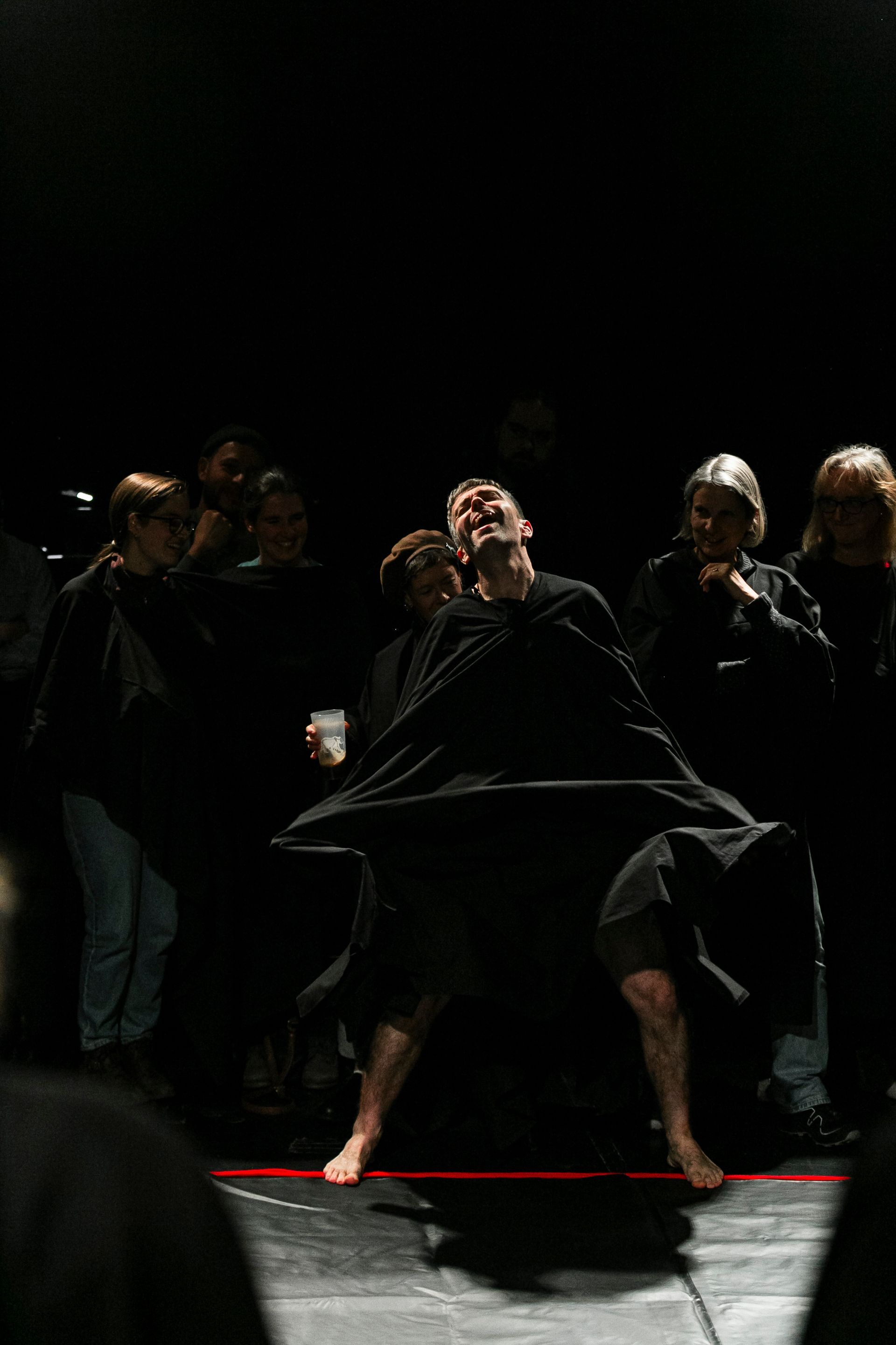 A group of people are standing around a man in a black cape on a stage.