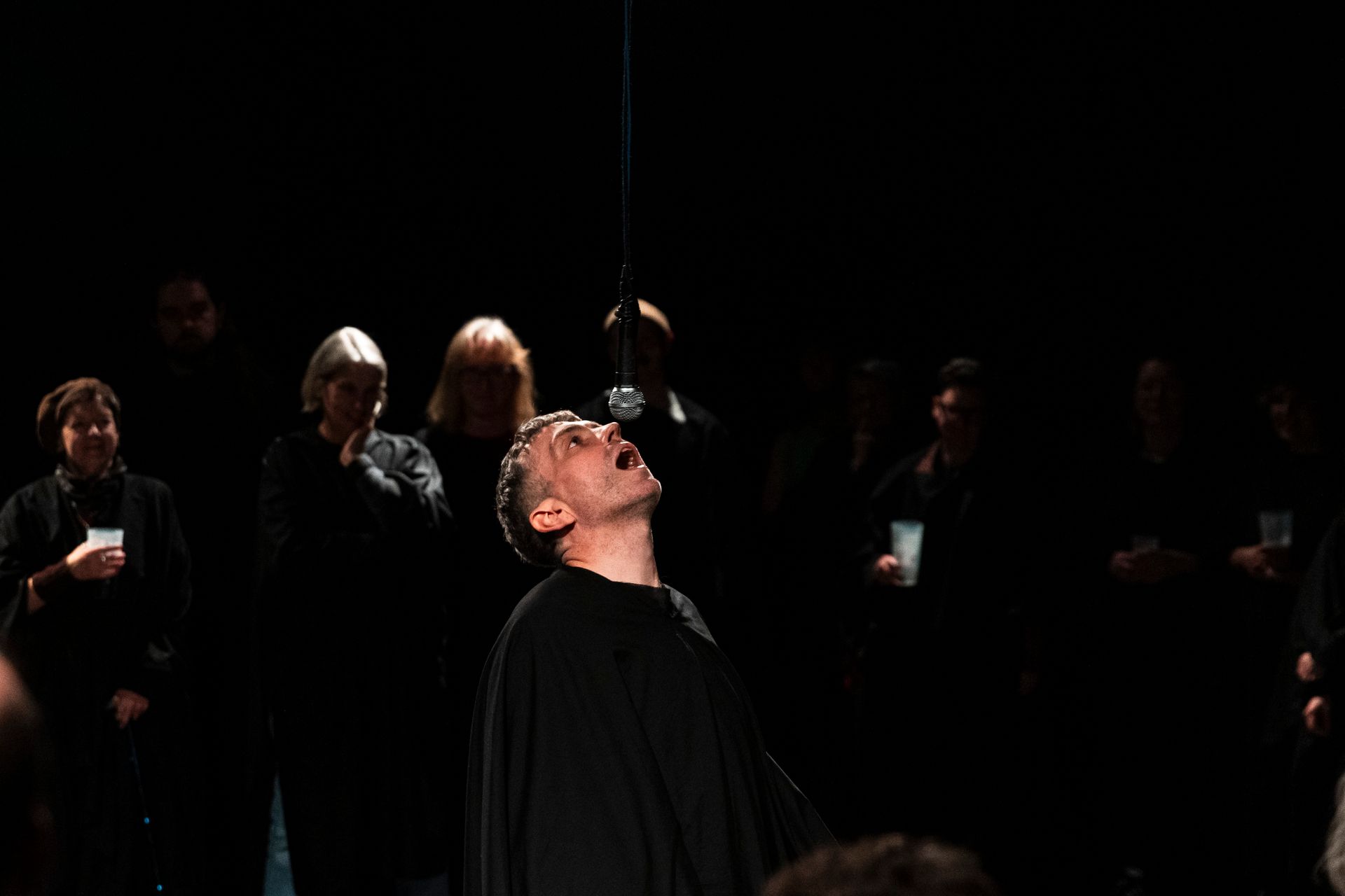 A man in a black cape is standing in front of a group of people in a dark room.