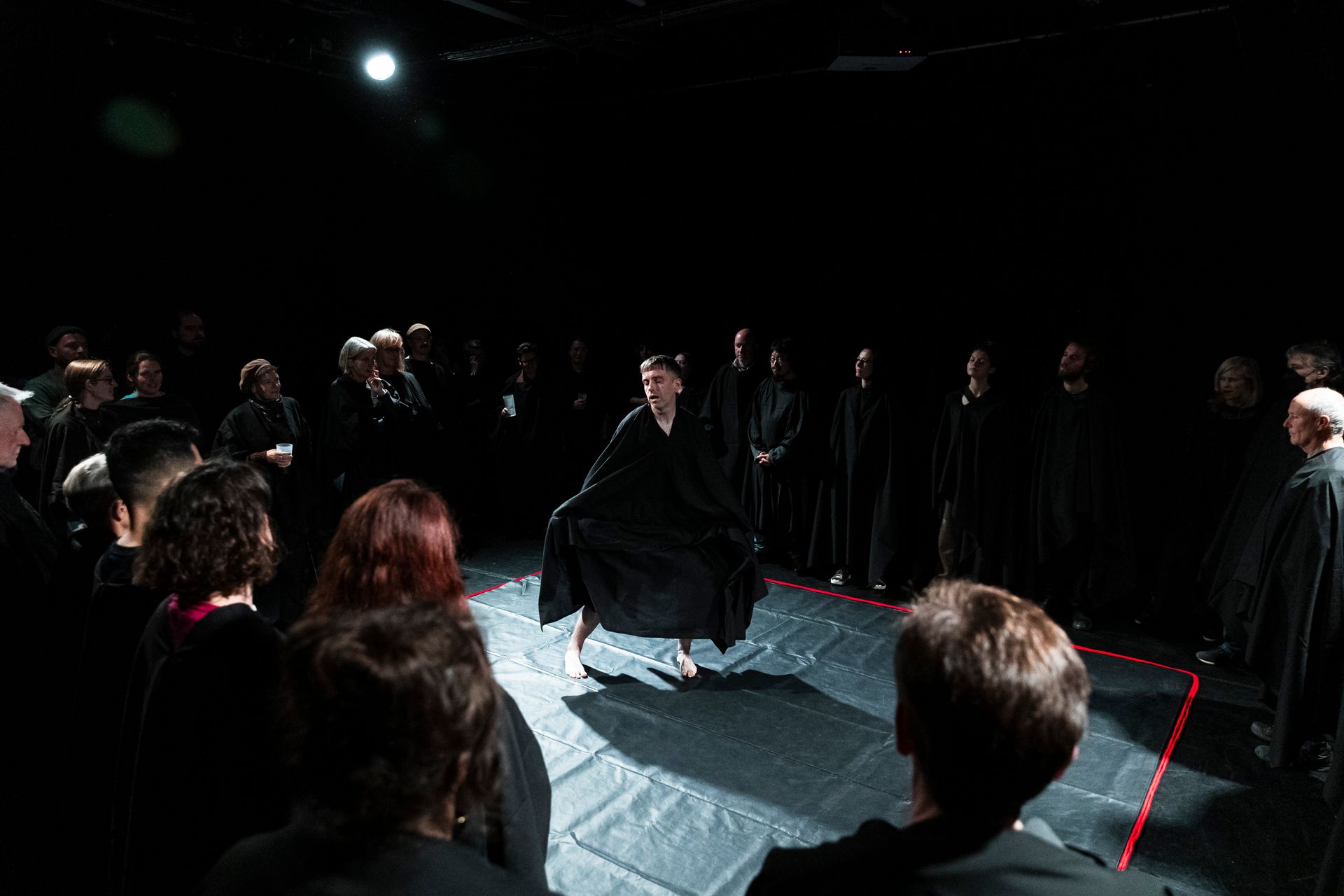 A group of people are standing around a man in a black robe on a stage.