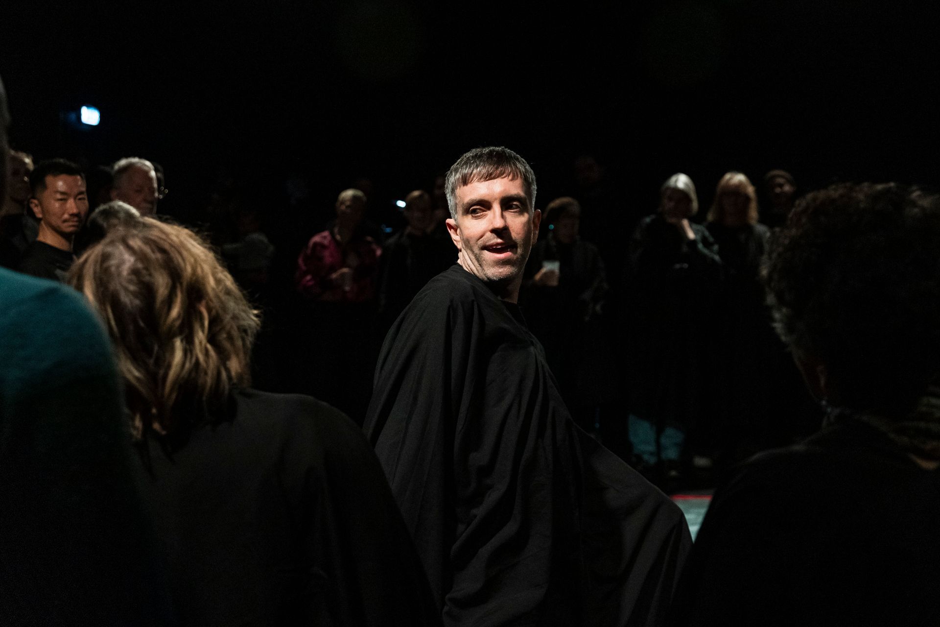 A man in a black robe is standing in a crowd of people in a dark room.