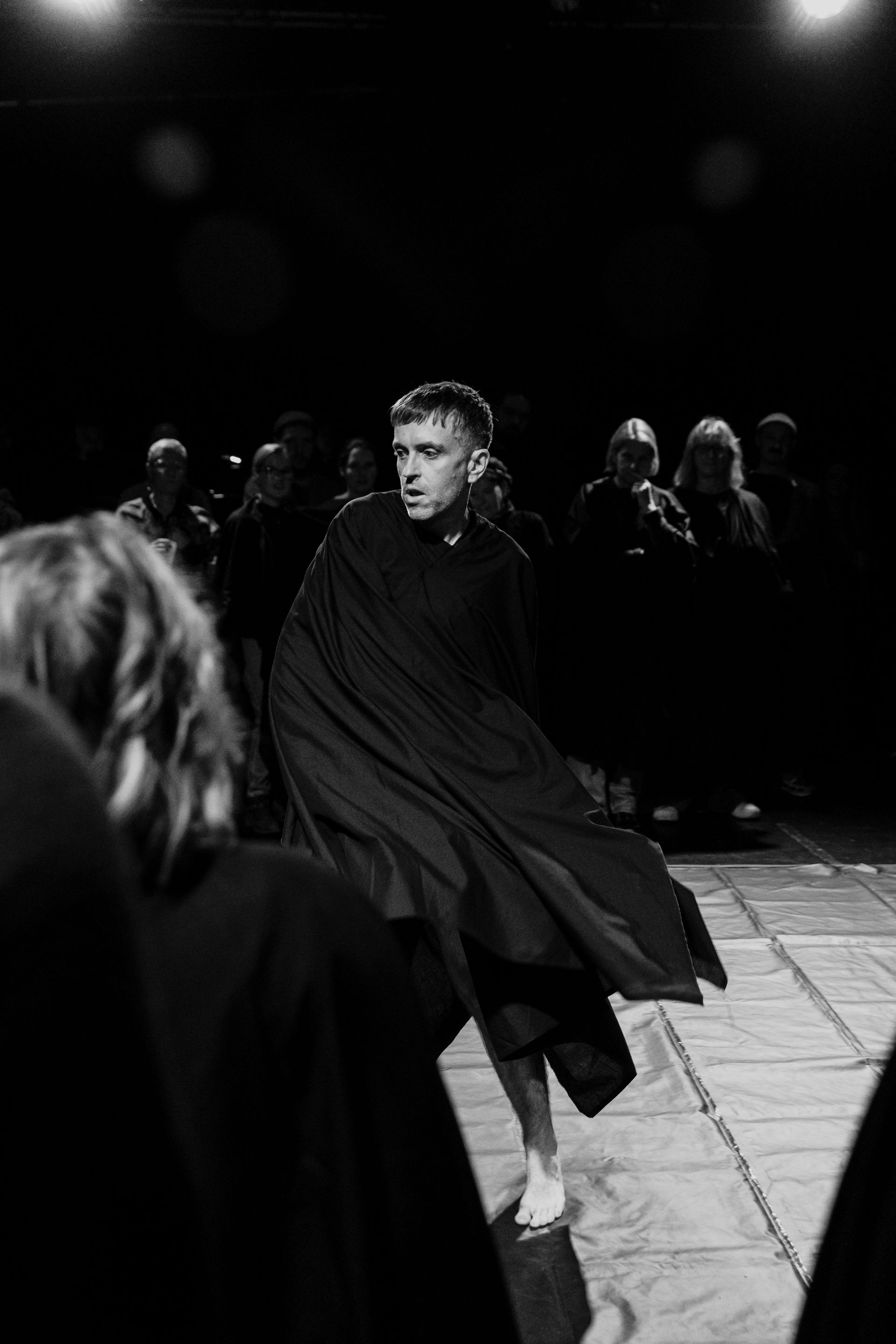 A man in a black cape is dancing on a stage in a black and white photo.