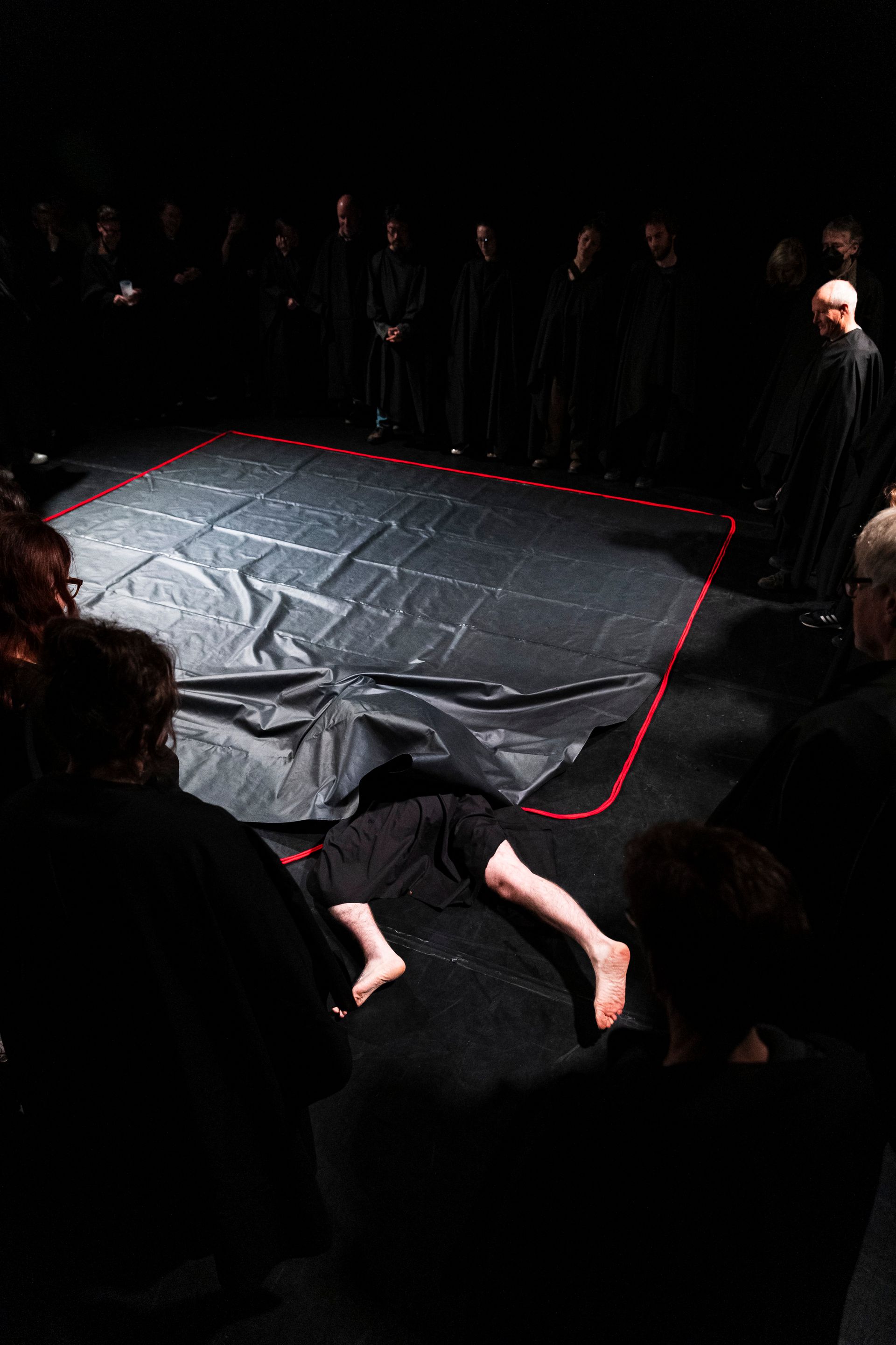 A man is laying under a black mat in a dark room.