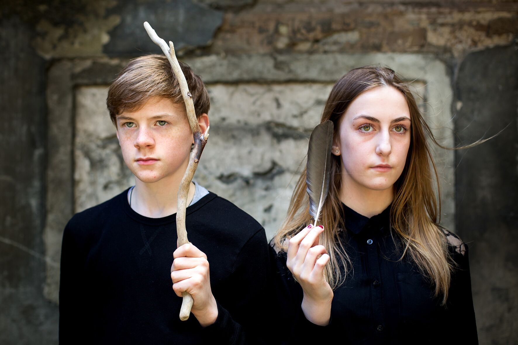 a boy and a girl are standing next to each other holding sticks and feathers .
