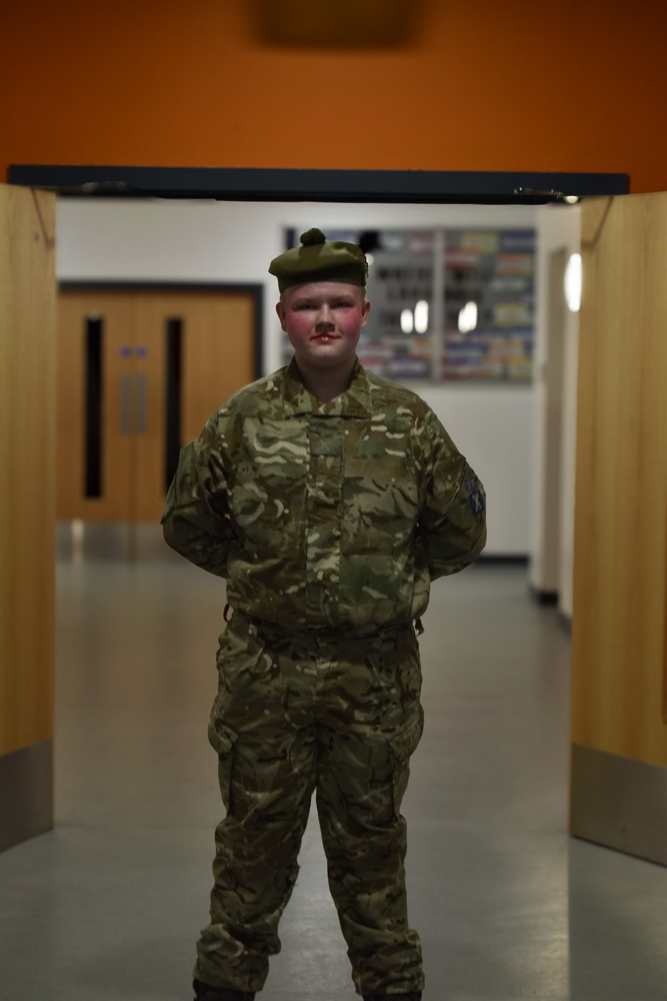 A boy in a military uniform is standing in a hallway.