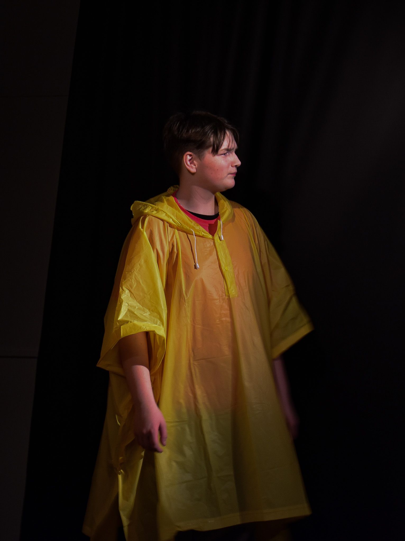 A boy wearing a yellow raincoat is standing in the dark.