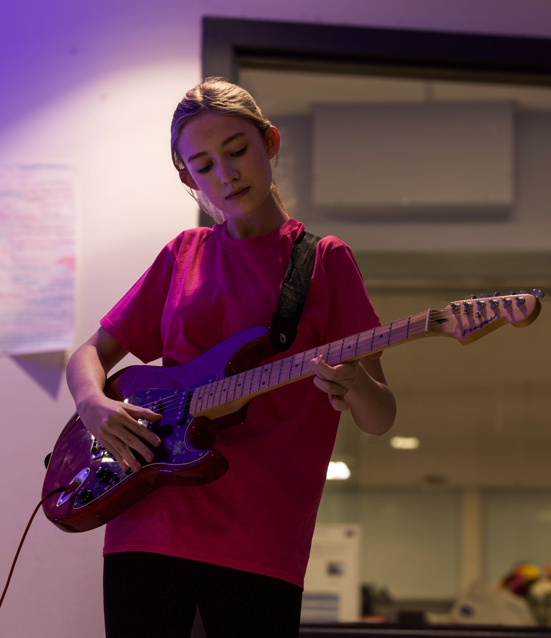 A girl in a pink shirt is playing an electric guitar.