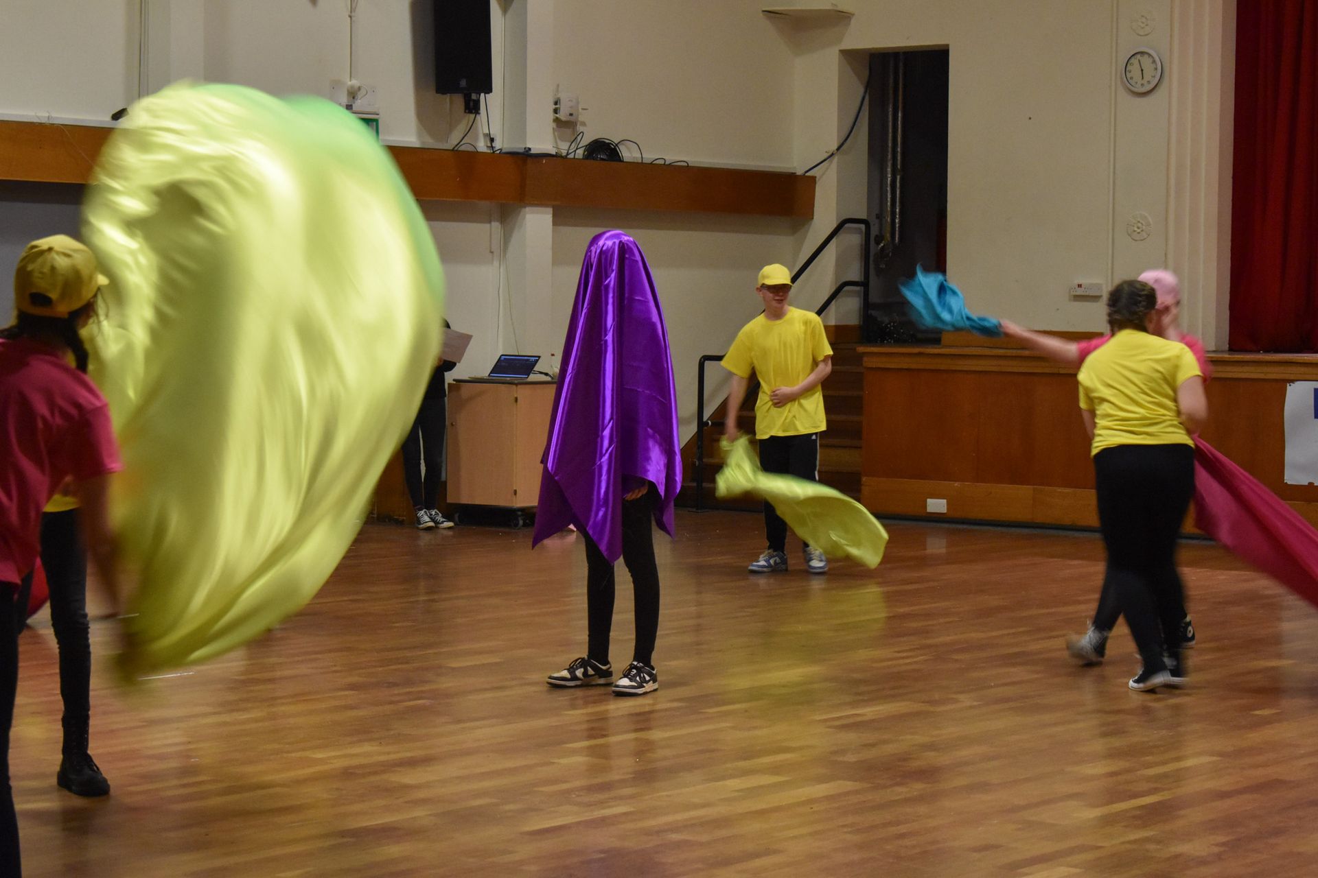 A group of people are standing on a wooden floor holding flags.