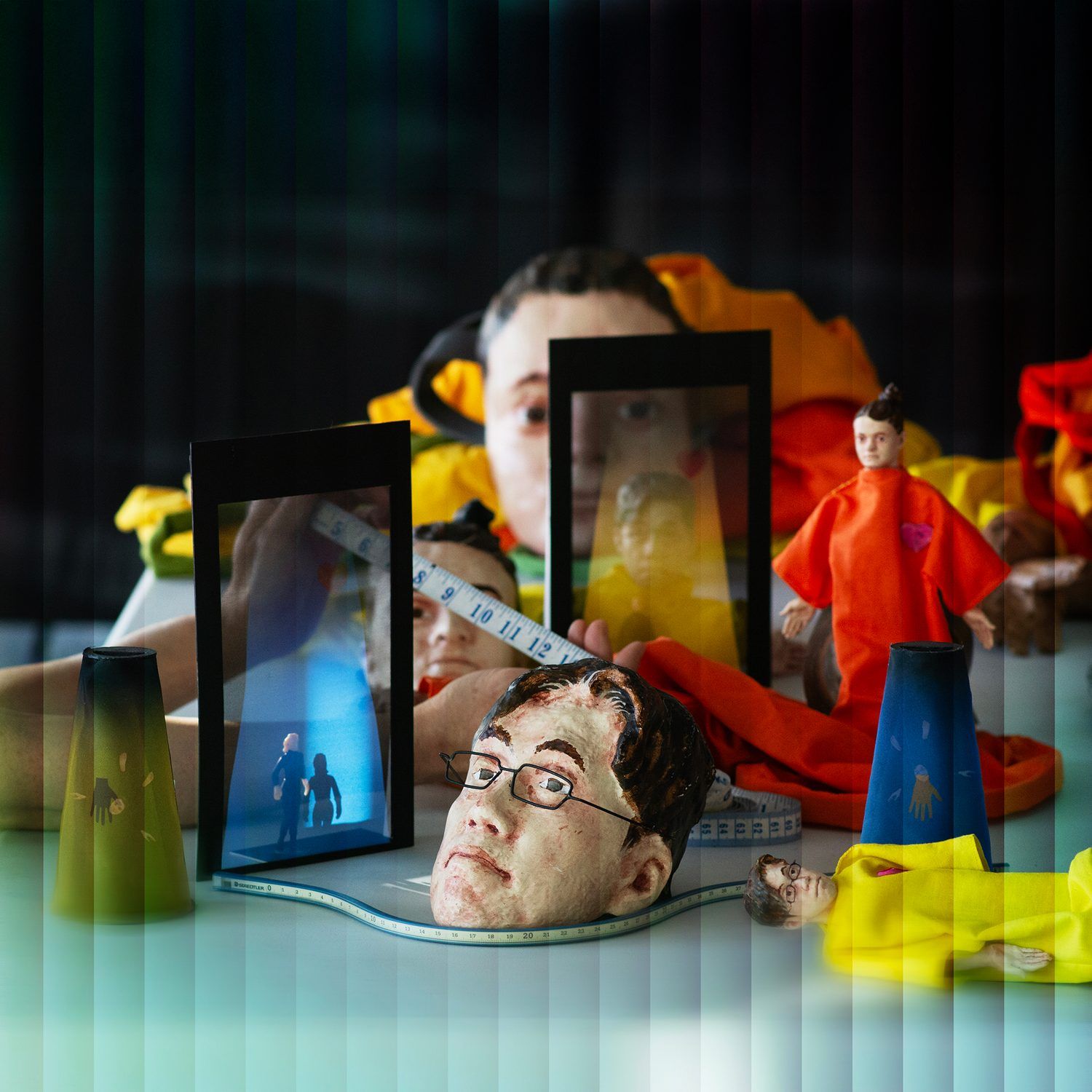 A collage with a figure holding up two smartphone-like screens with images of two people and multiple figurines.