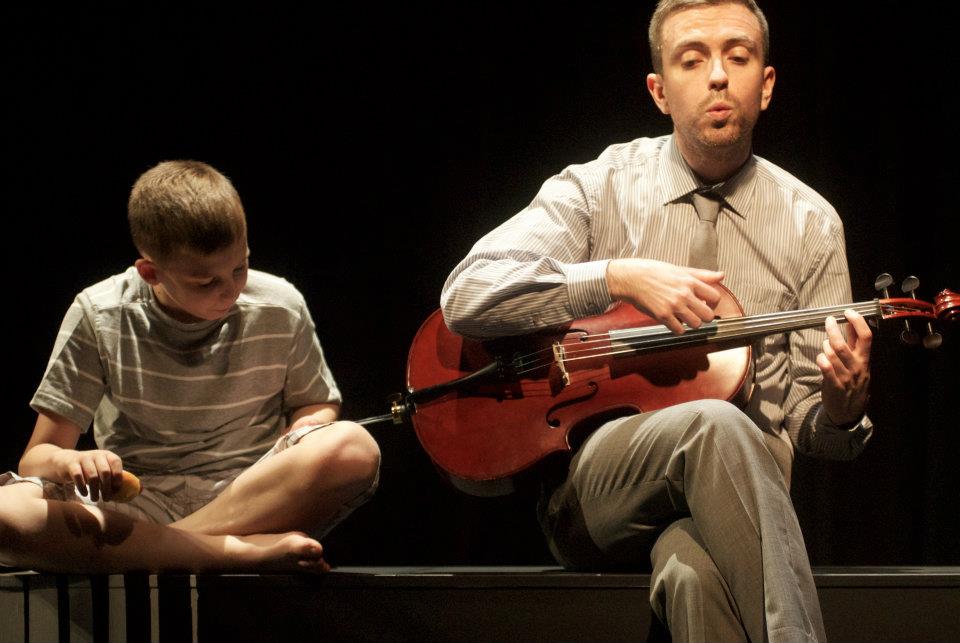 a man is playing a violin while a boy sits next to him