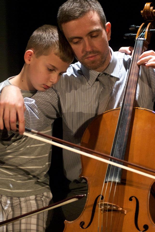 a man is teaching a young boy how to play a cello .