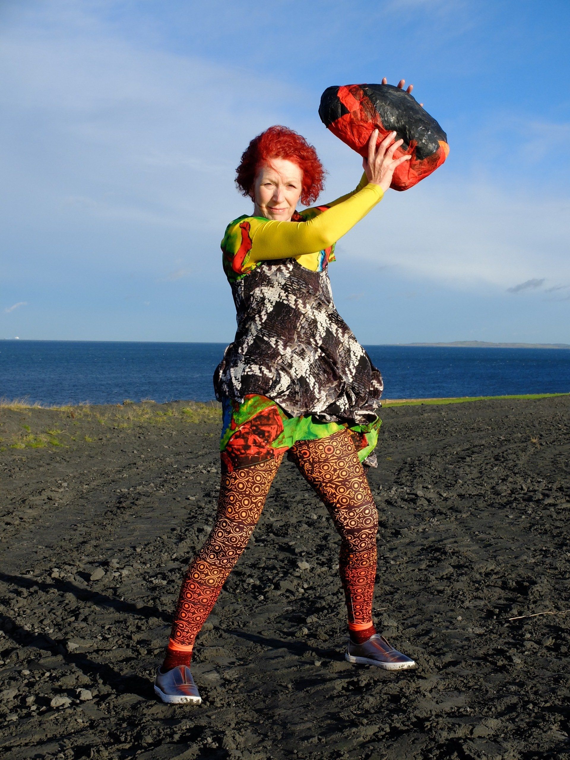 a woman in a colorful dress is holding a red rock over her head