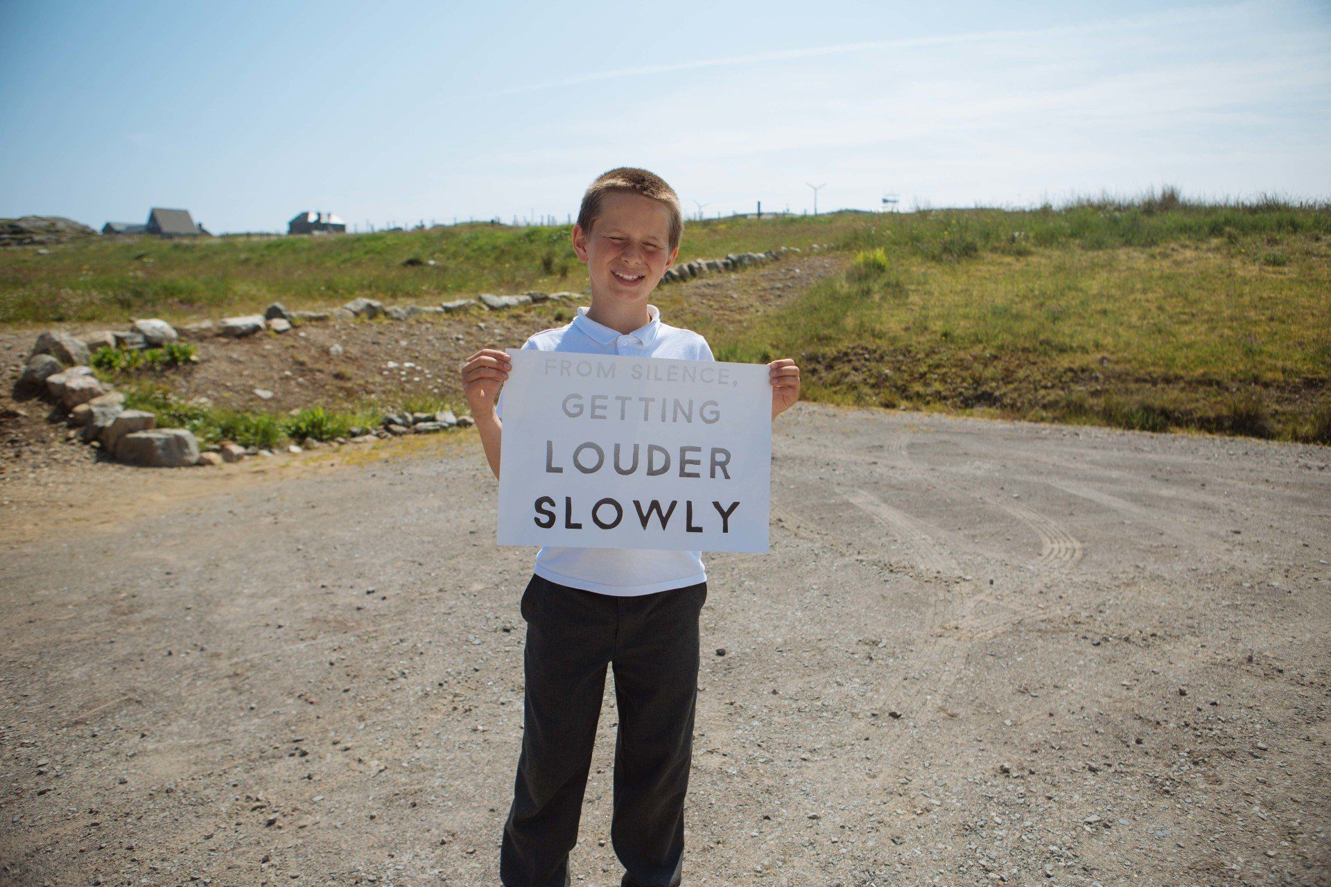 a young boy is holding a sign that says getting louder slowly