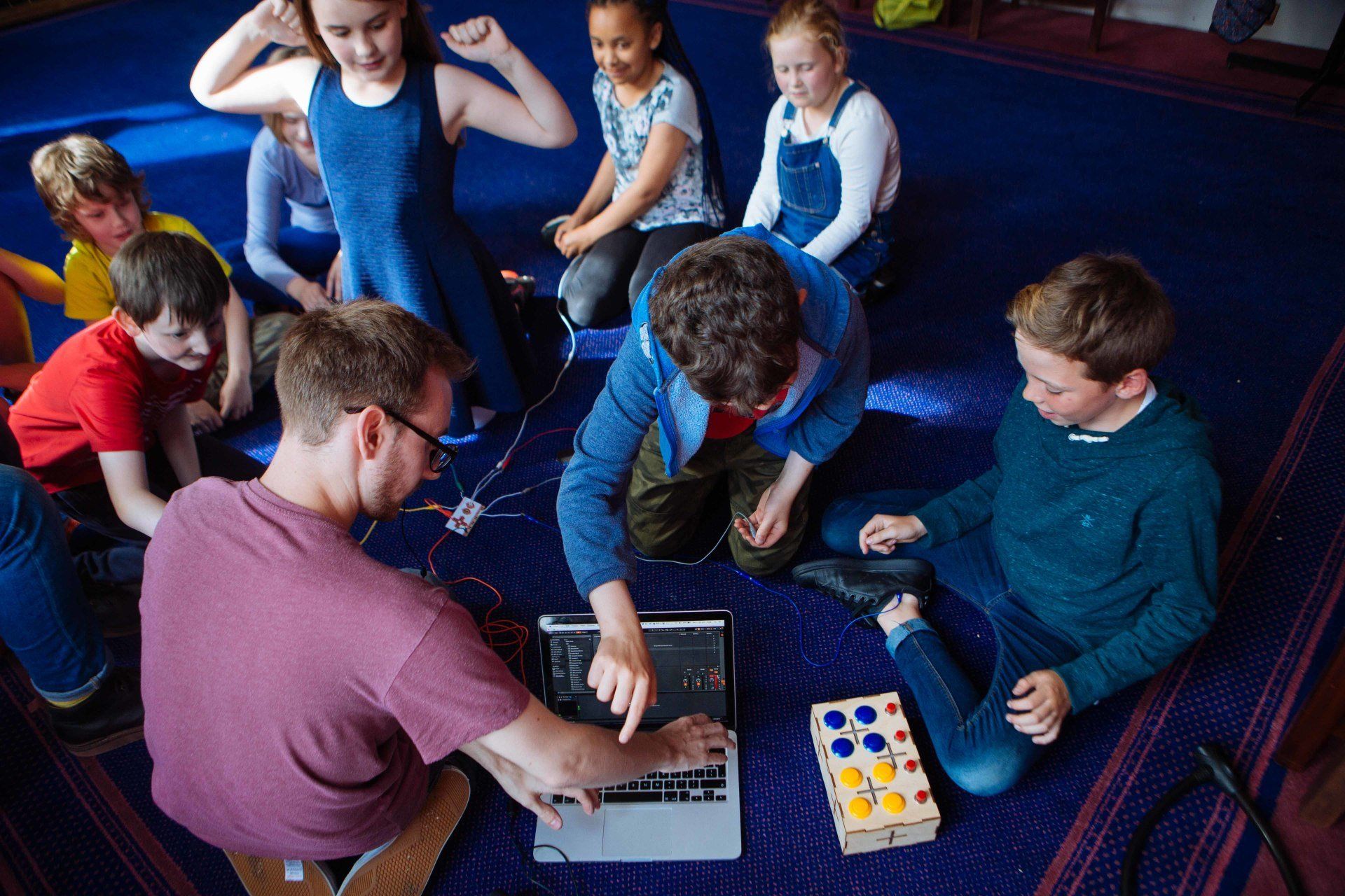 a group of children are sitting on the floor playing with a laptop computer .
