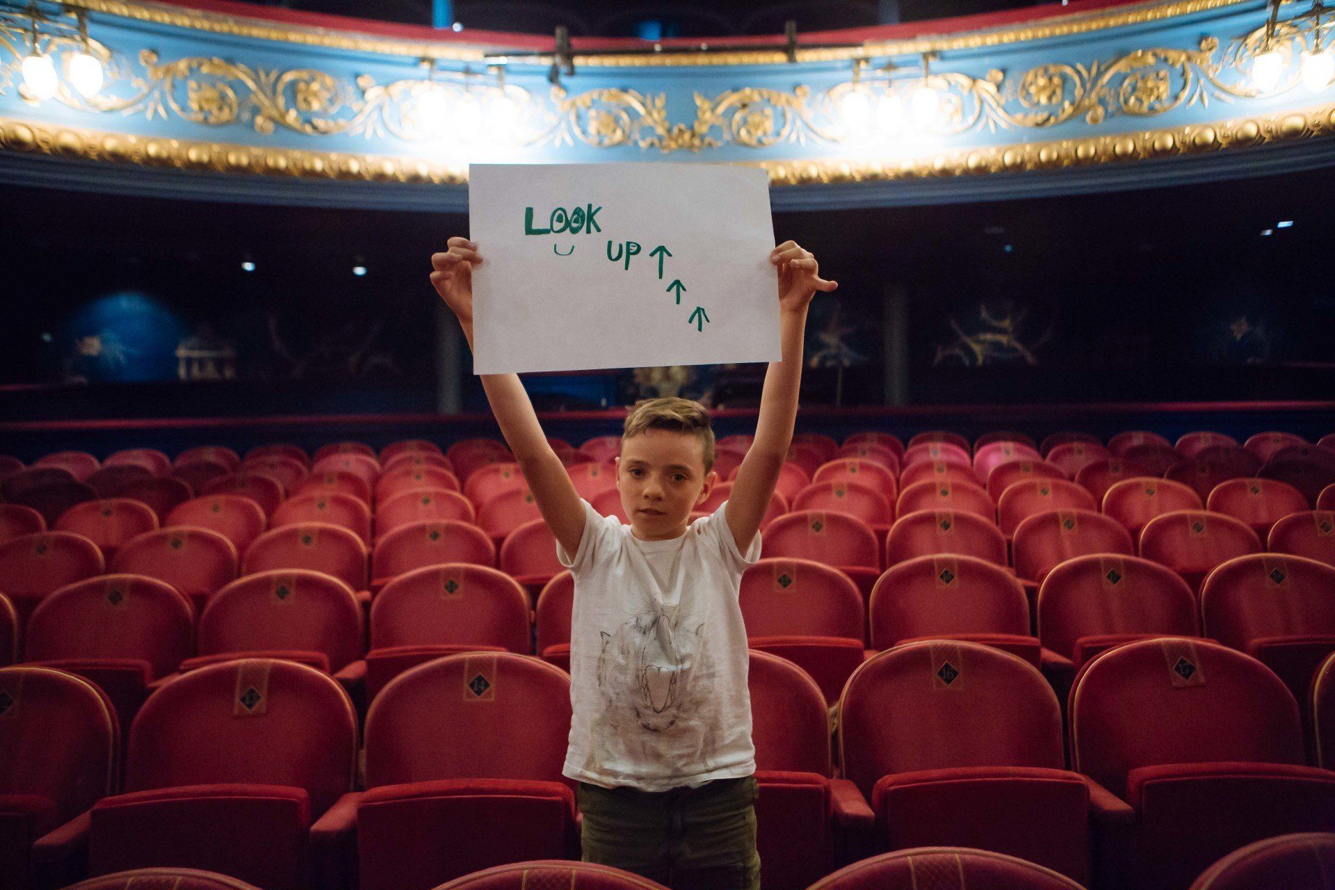 a young boy is holding a sign in an empty auditorium .
