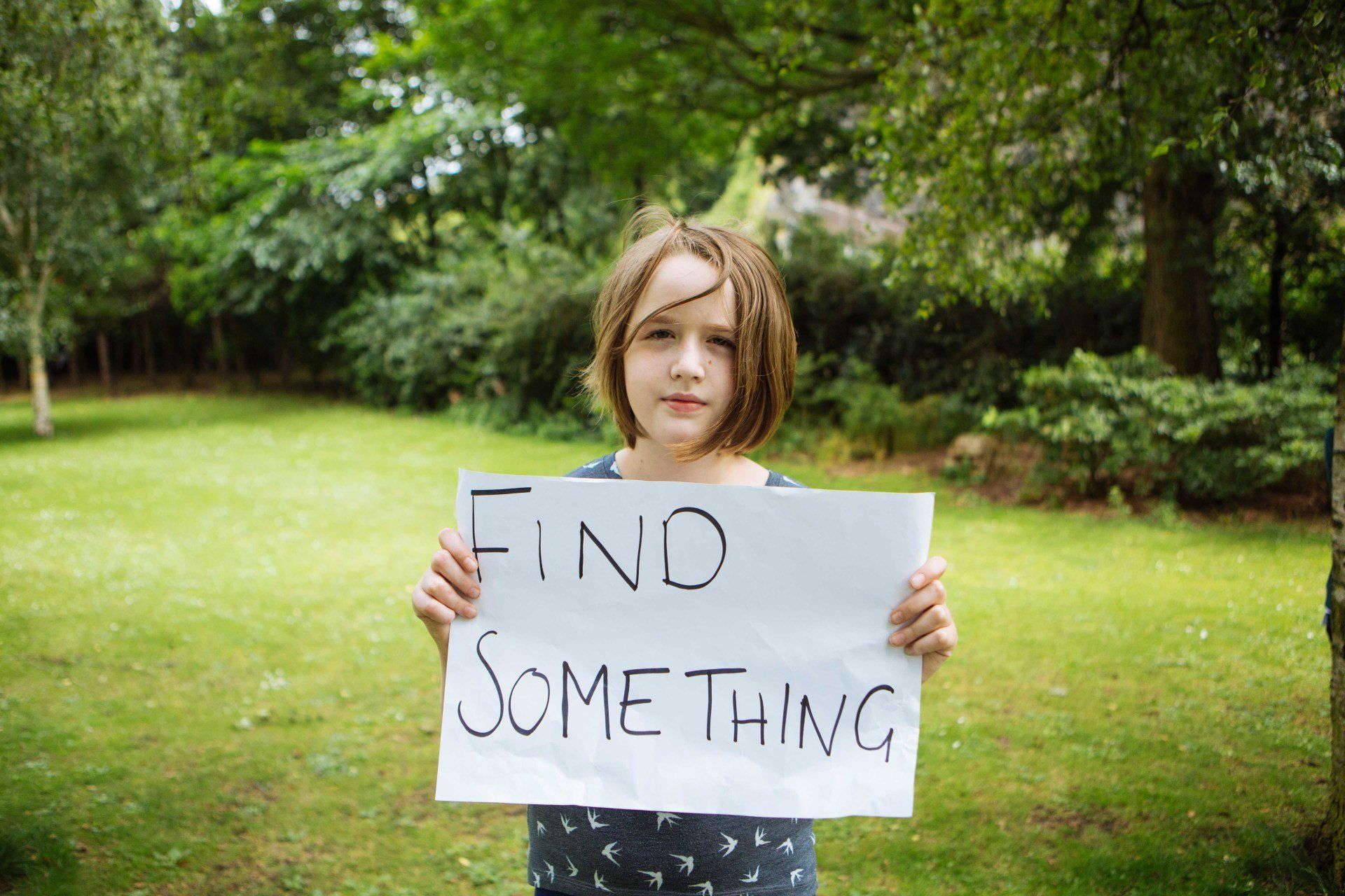 a young girl is holding a sign that says `` find something '' .