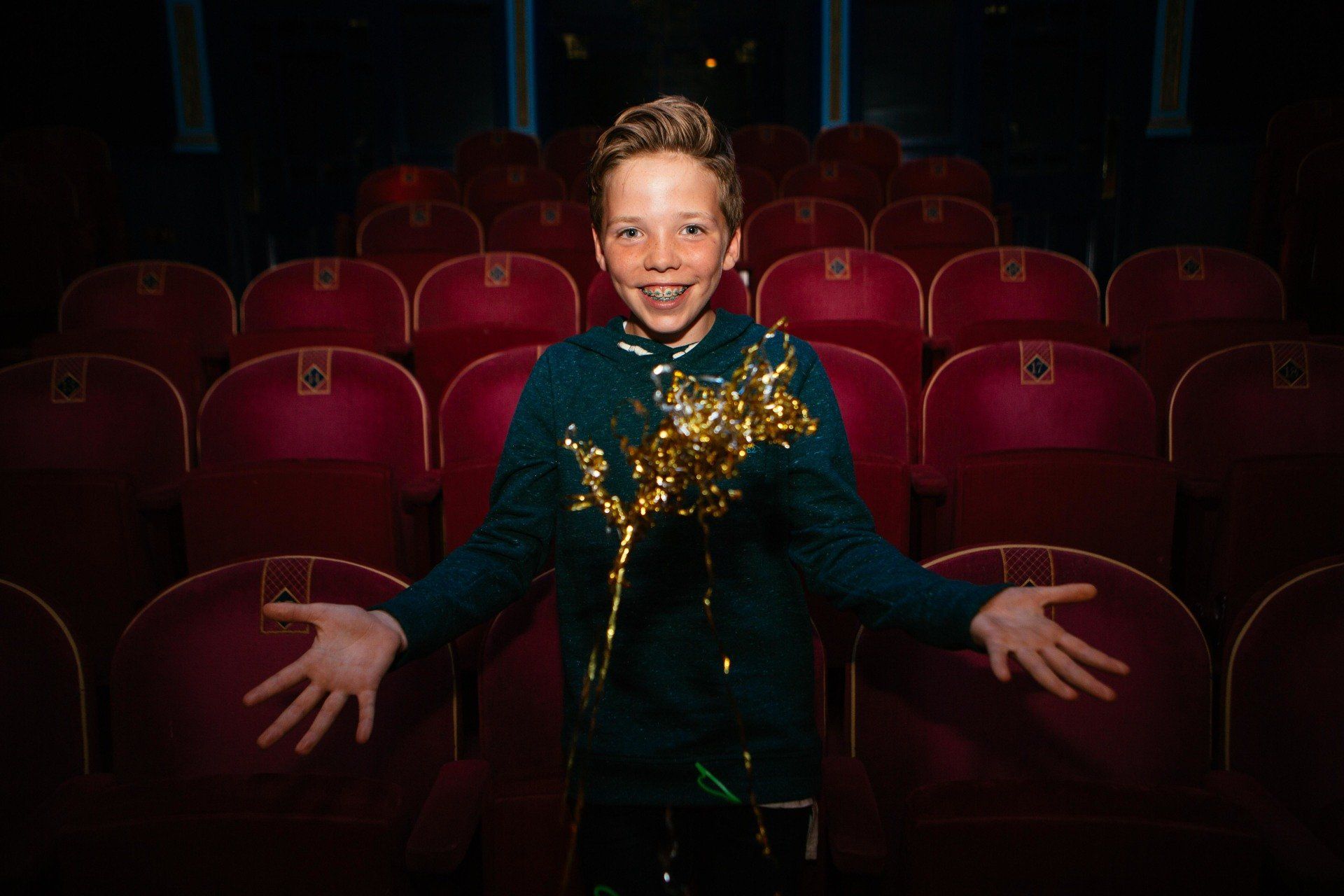 a young boy is standing in a theater holding a piece of gold confetti .