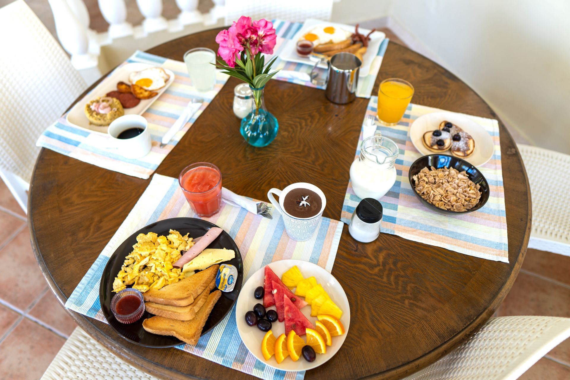Desayuno servido en una mesa redonda de madera, que incluye huevos, tostadas, fruta, avena, jugo y café.