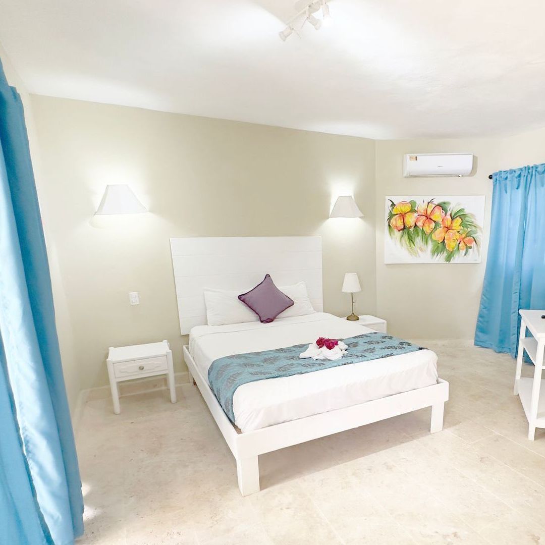 Dormitorio con cama blanca, mesita de noche, cortinas azules y arte de pared.