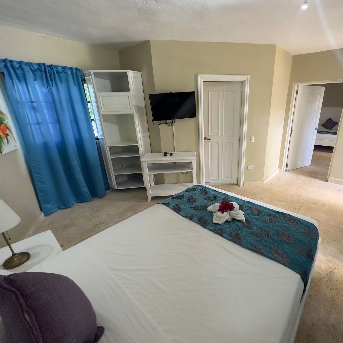 Dormitorio con una cama blanca, detalles en verde azulado, un televisor y un armario blanco.