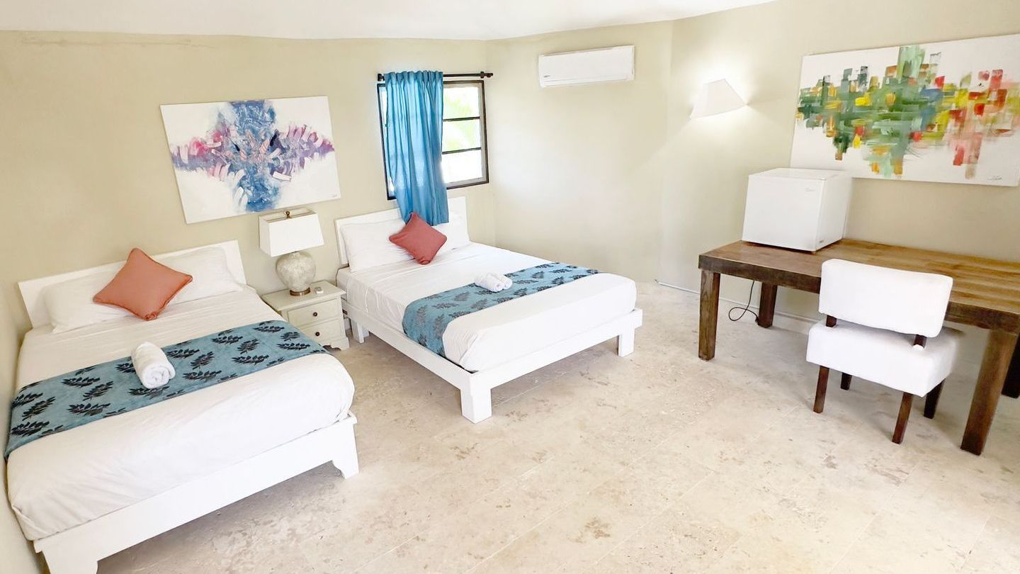 Dormitorio con dos camas blancas, un escritorio y obras de arte coloridas en las paredes.