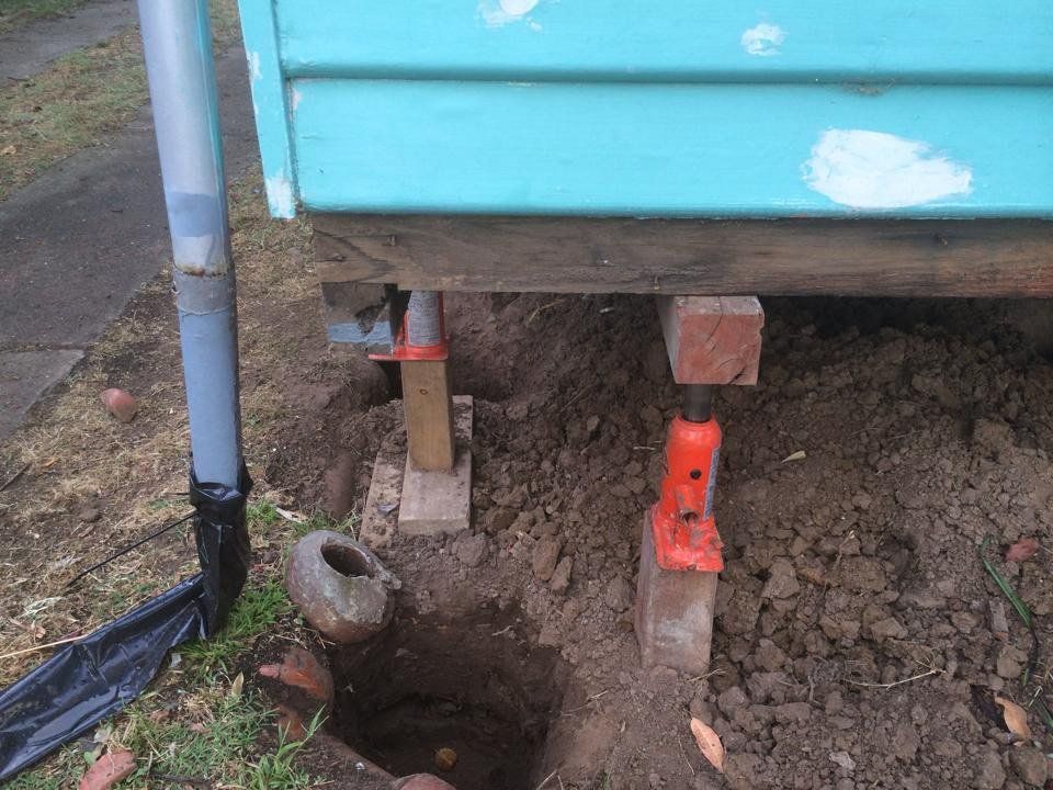 A Blue House is Being Lifted by a Jack in the Dirt — Melbourne, VIC — Special Reblocking Services