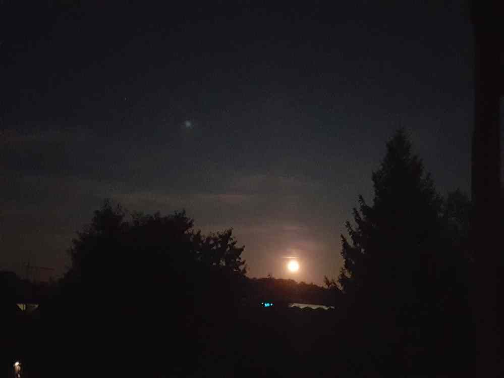 Dark night sky with a bright moon and a smaller light above it; trees in silhouette.